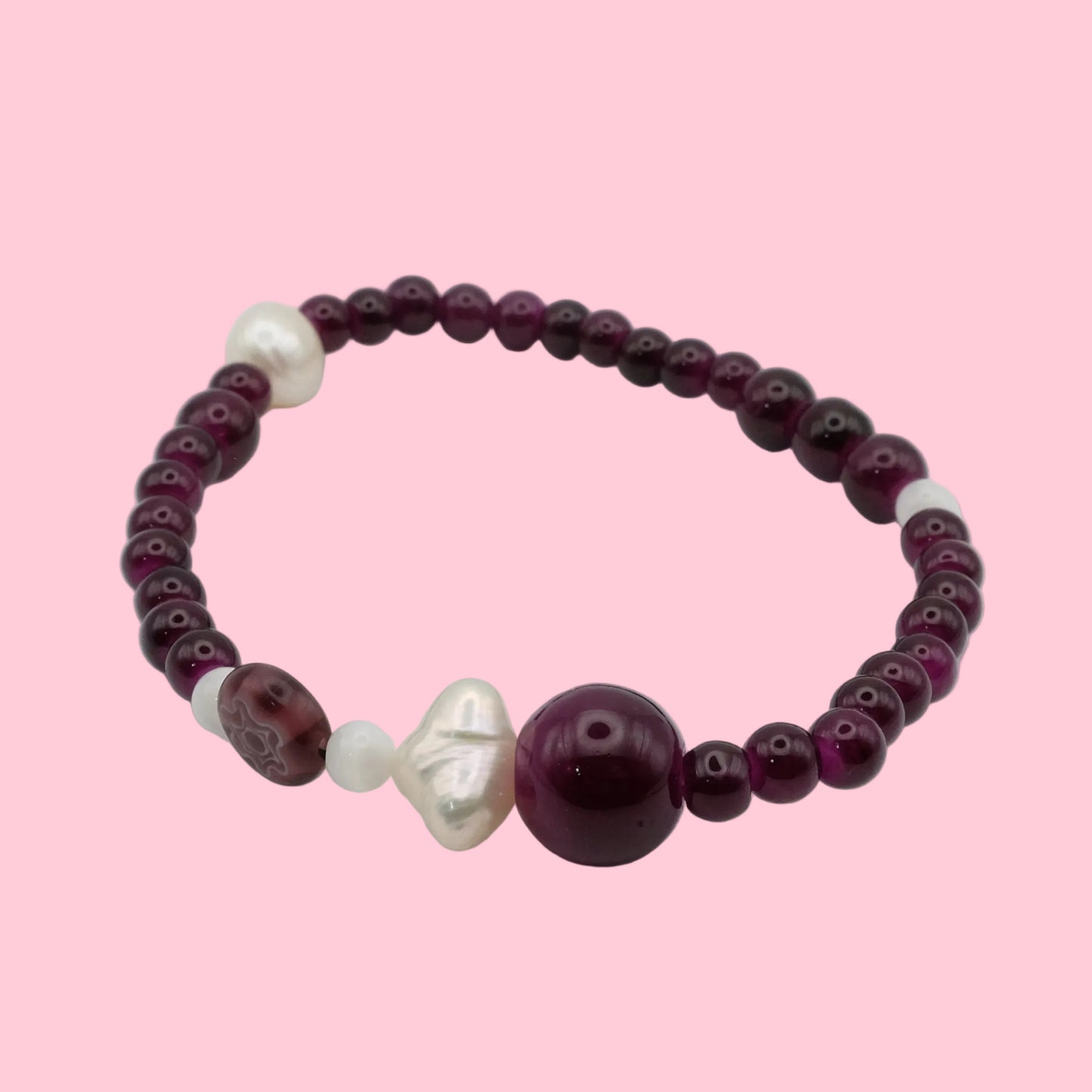 An elastic beaded bracelet composed of deep wine glass beads in mixed sizes, featuring freshwater pearls, mother of pearl accent beads and a floral lampwork bead, shown on a white background.