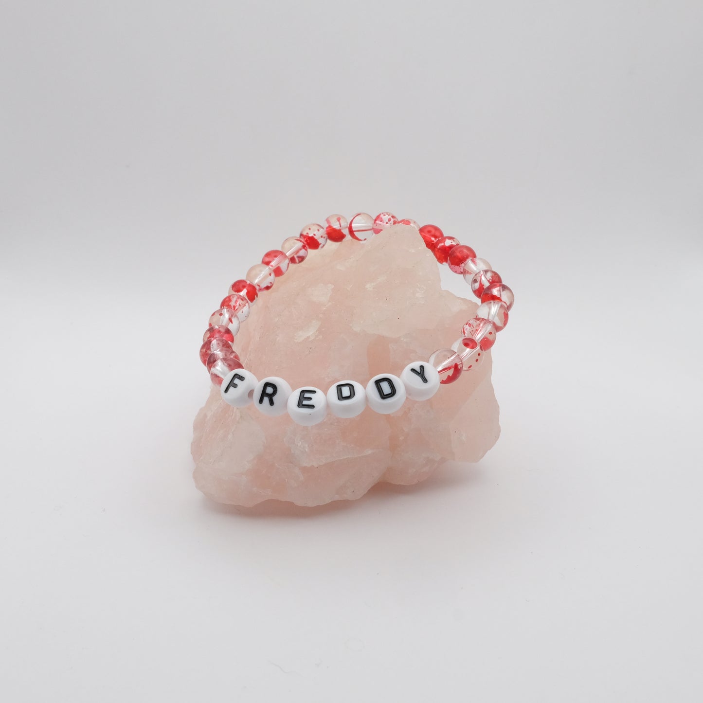 Bracelet with red and clear beads and letter beads spelling 'FREDDY' on a pink stone.
