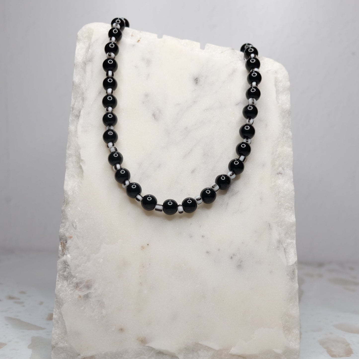 Black beaded necklace on a white marble stand against a light gray background