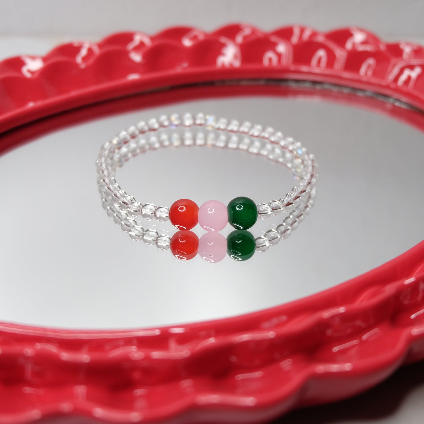 A beaded bracelet with red, green, and pink beads on a red tray.