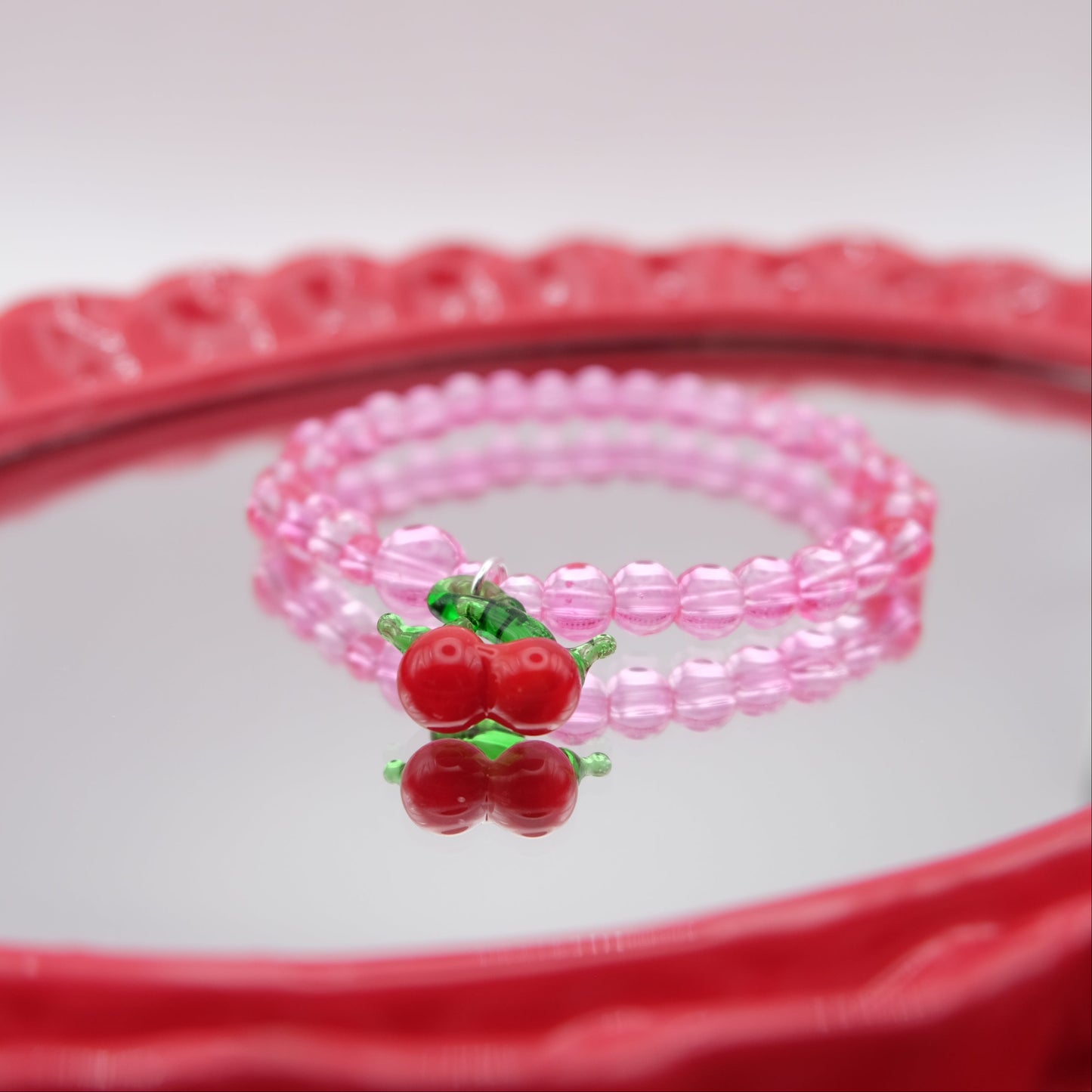 Pink beaded bracelet with cherry charm on a red and white background