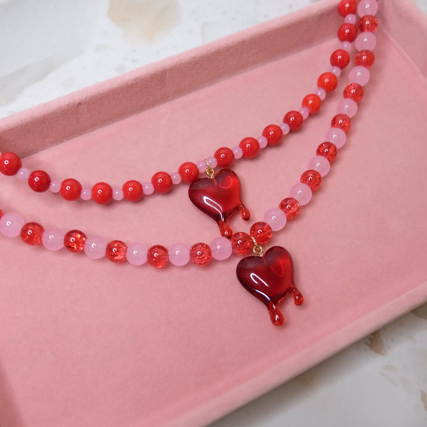 Beaded necklace with red heart pendants on a pink tray