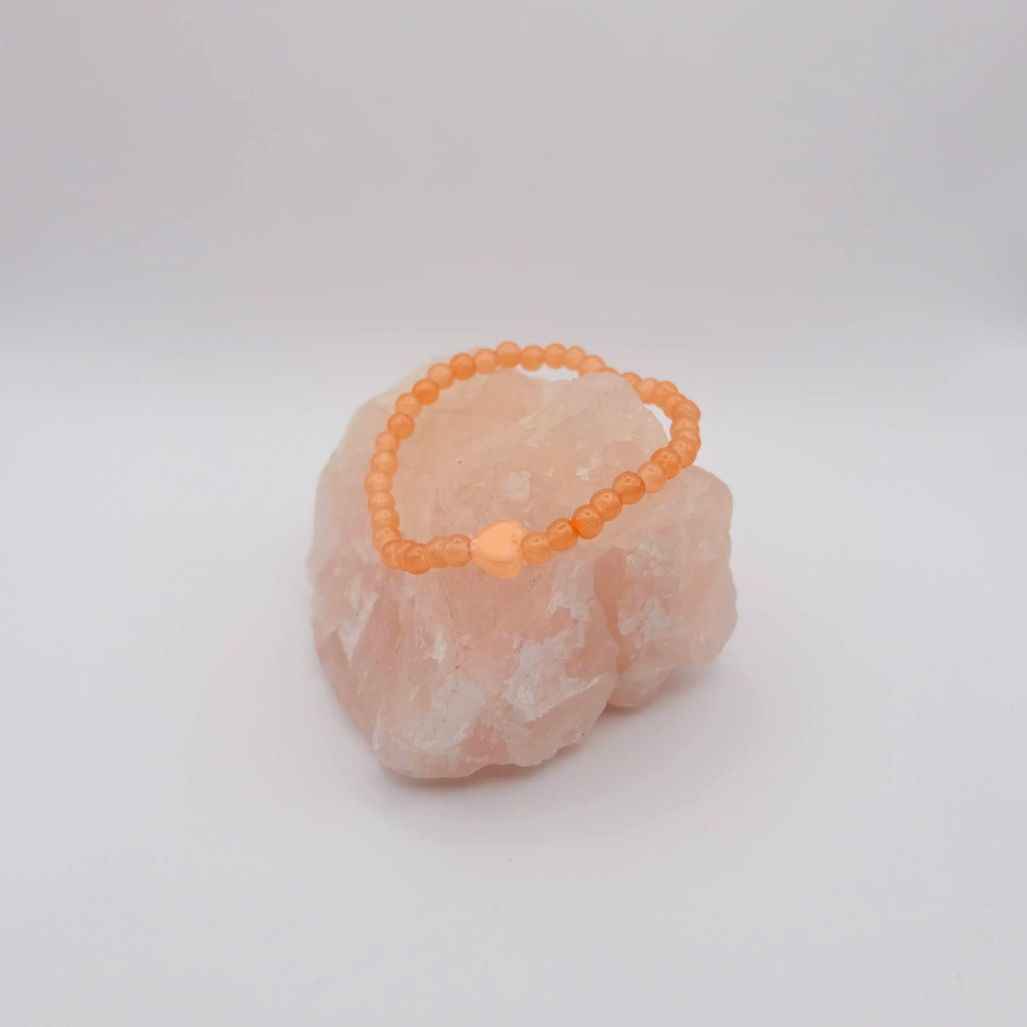 Orange beaded bracelet on a pink stone against a white background