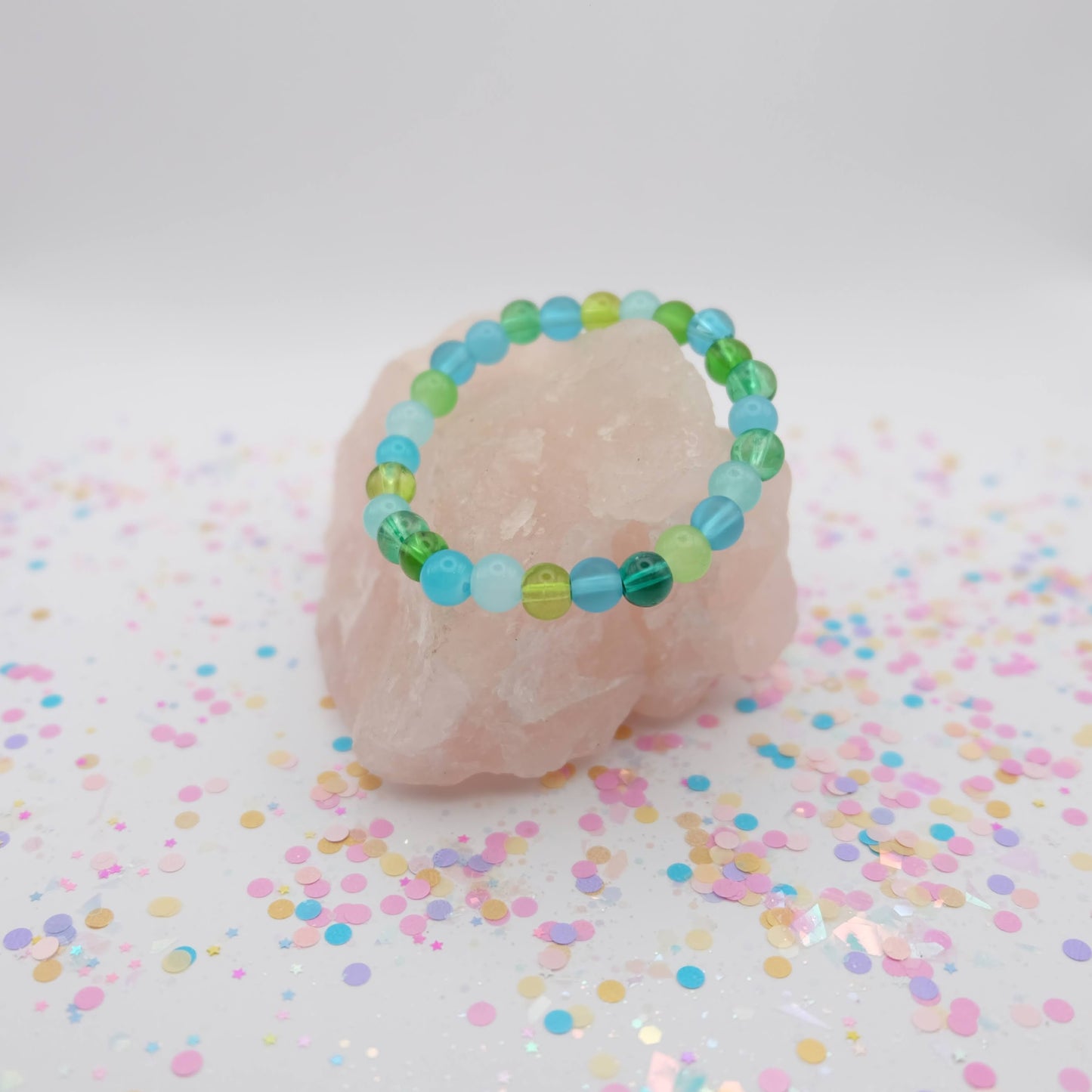 Green, aqua and blue beaded bracelet on a pink stone with confetti background