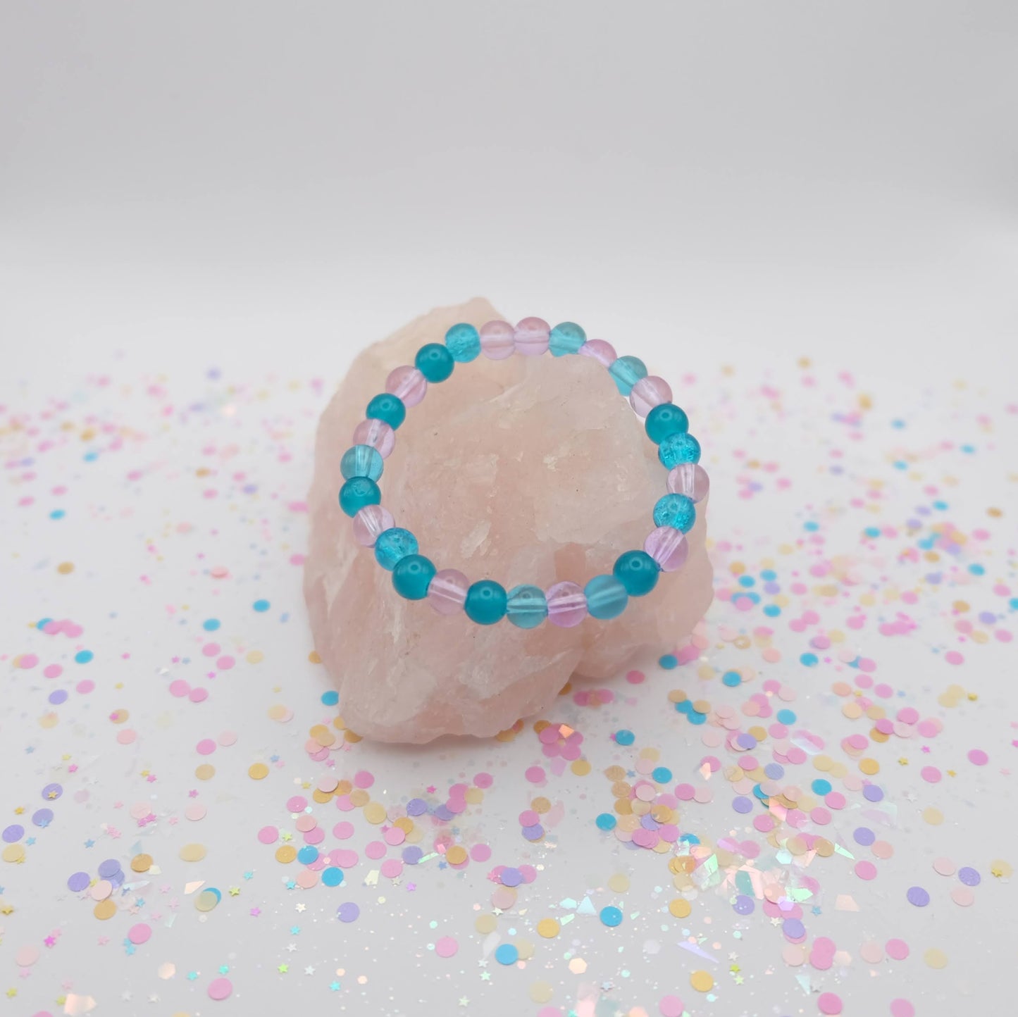 Turquoise and purple beaded bracelet on a pink stone with colorful confetti on a white background