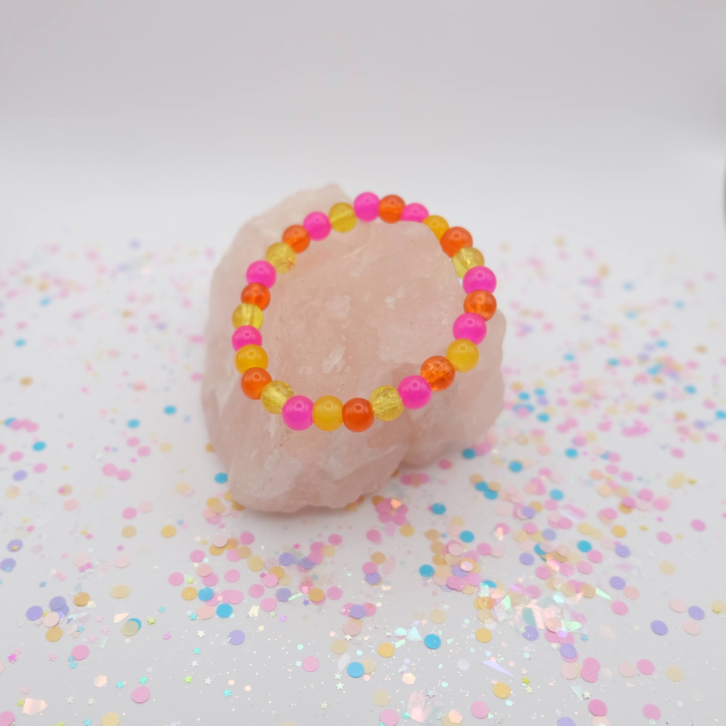 Pink, yellow and orange beaded bracelet on a pink rock with confetti background