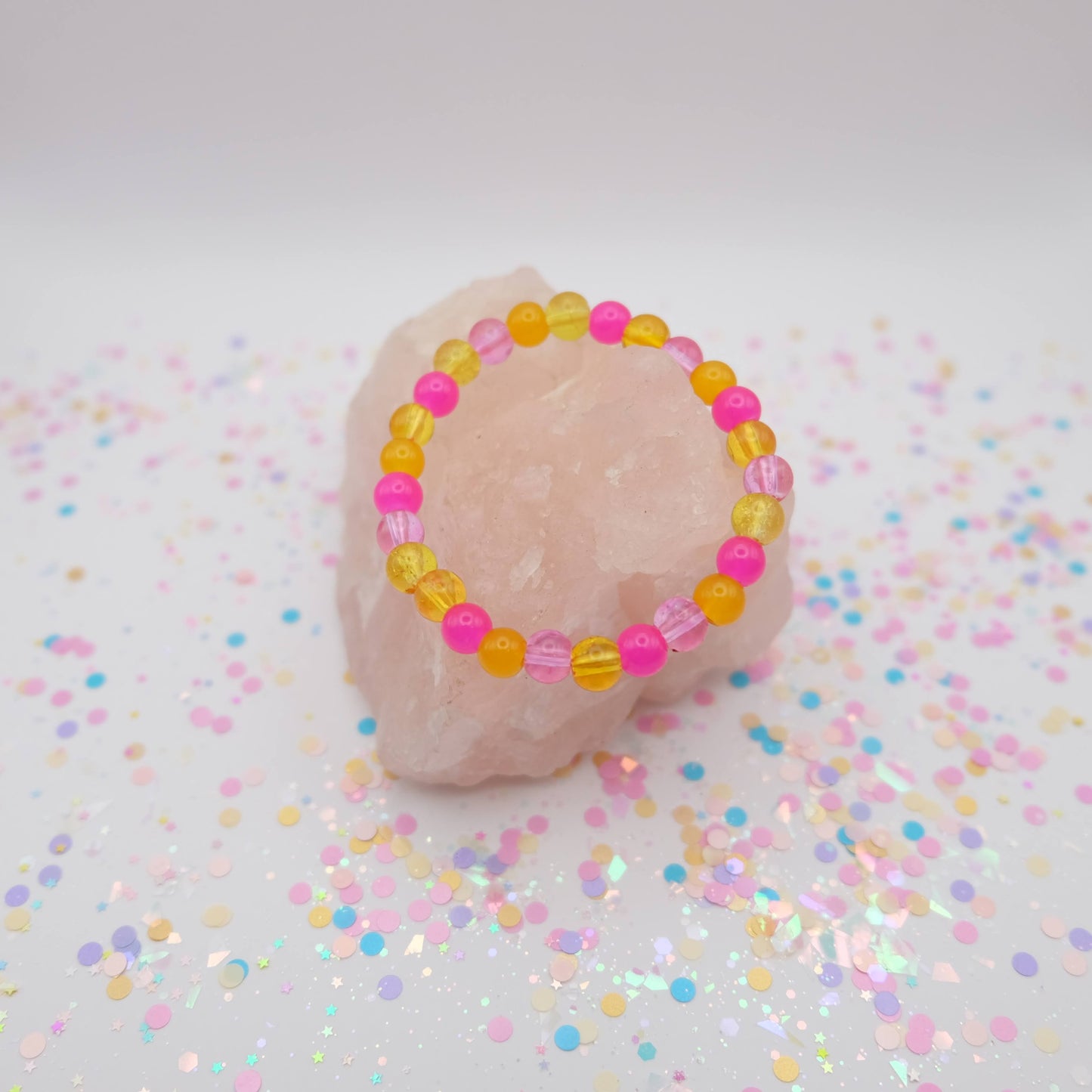 Pink and yellow beaded bracelet on a pink stone with confetti background
