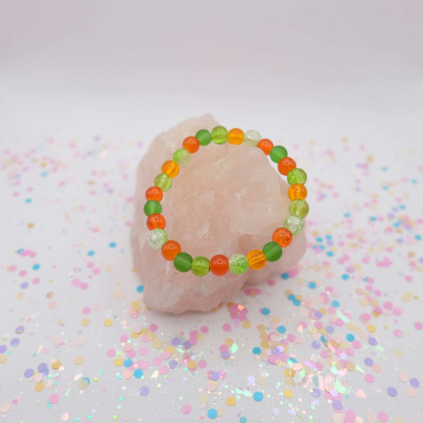 Green and orange beaded bracelet on a pink object with confetti background