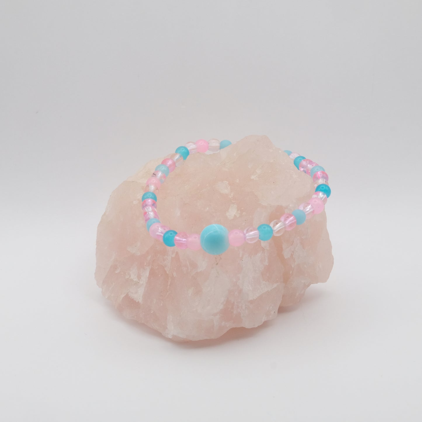 A single elastic beaded bracelet in pink and blue sitting on a rose quartz rock with a white background