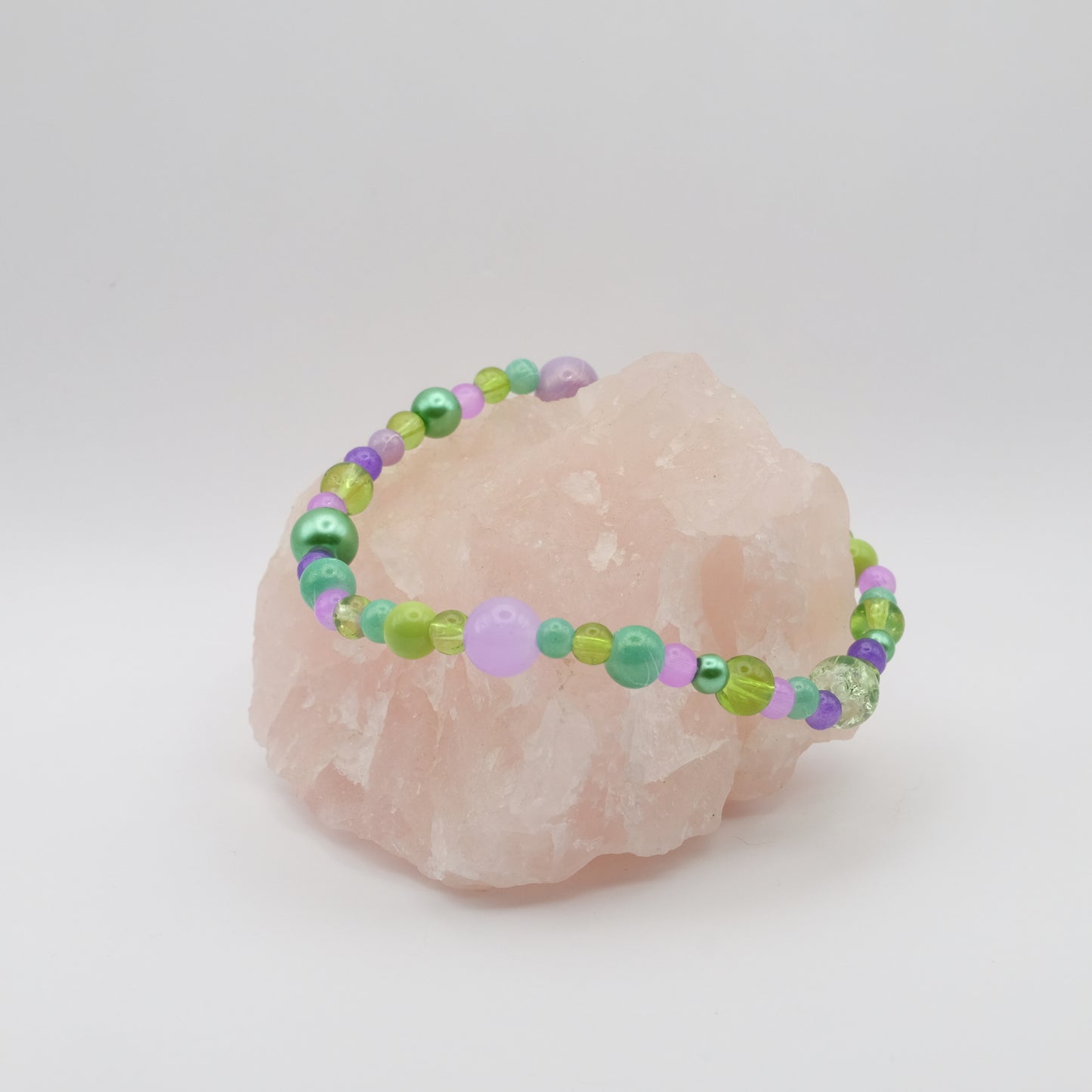 Beaded bracelet with green and purple beads on a pink stone against a white background