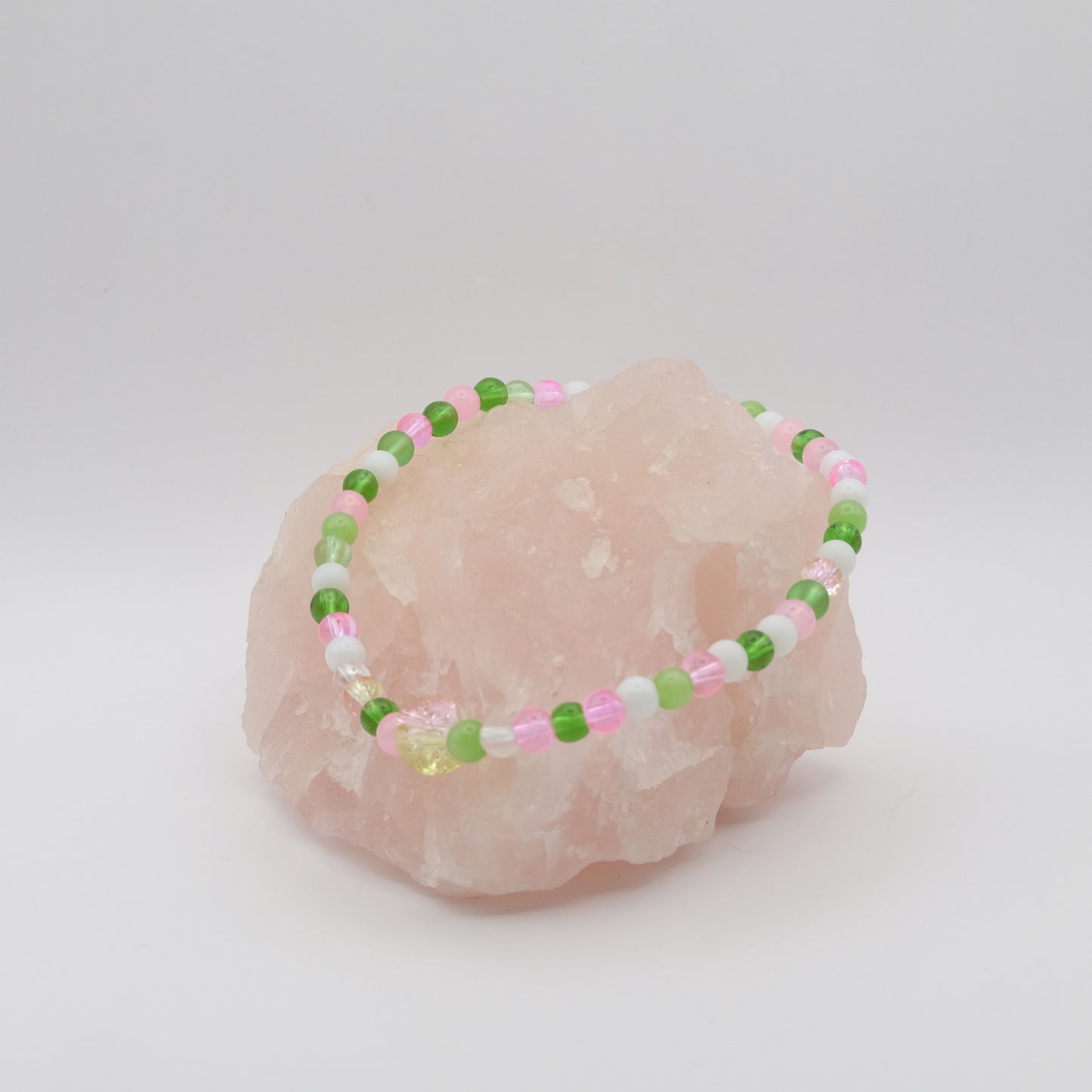 Beaded bracelet with green, pink, and white beads on a pink stone against a light gray background