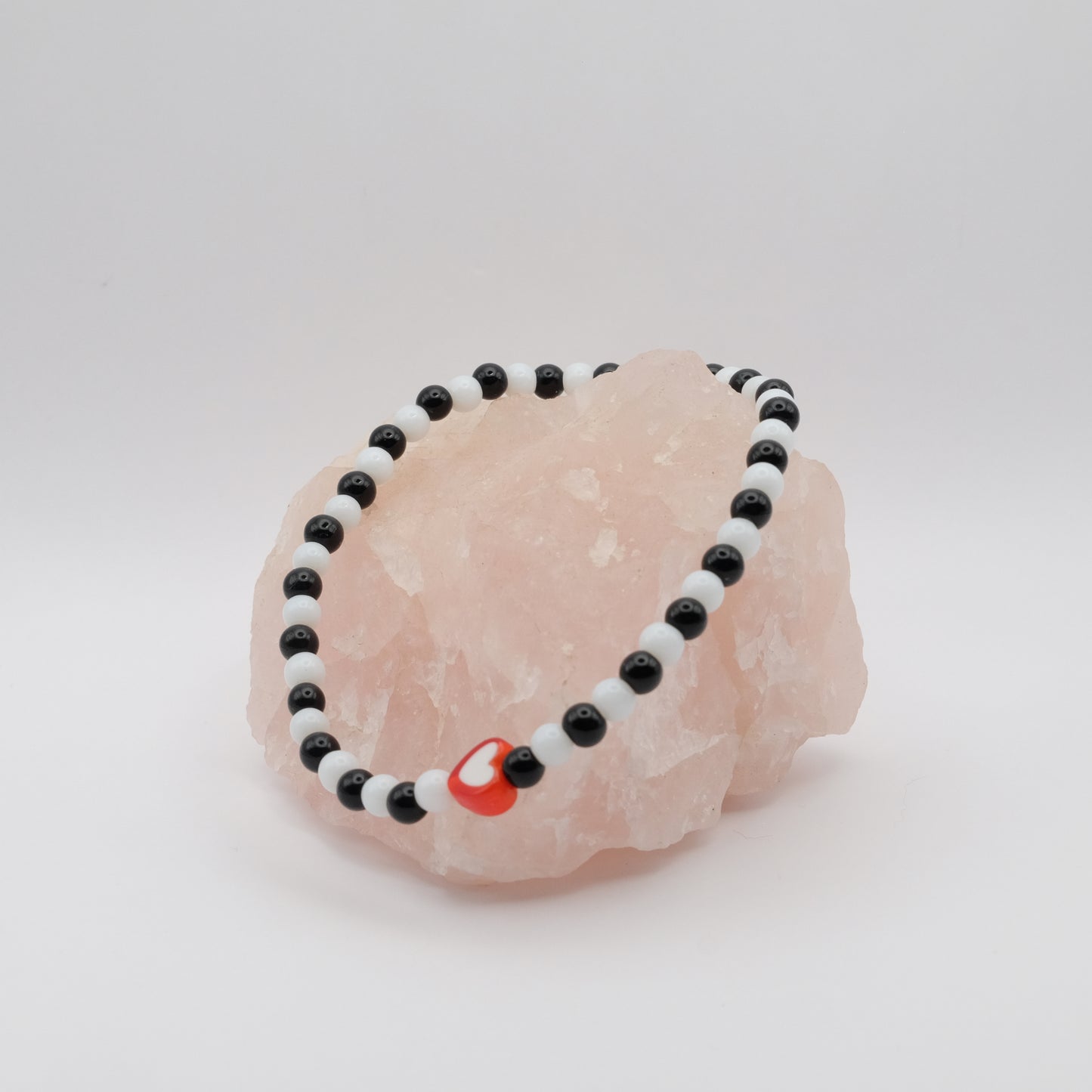 Black and white beaded bracelet with a red charm on a pink stone against a white background