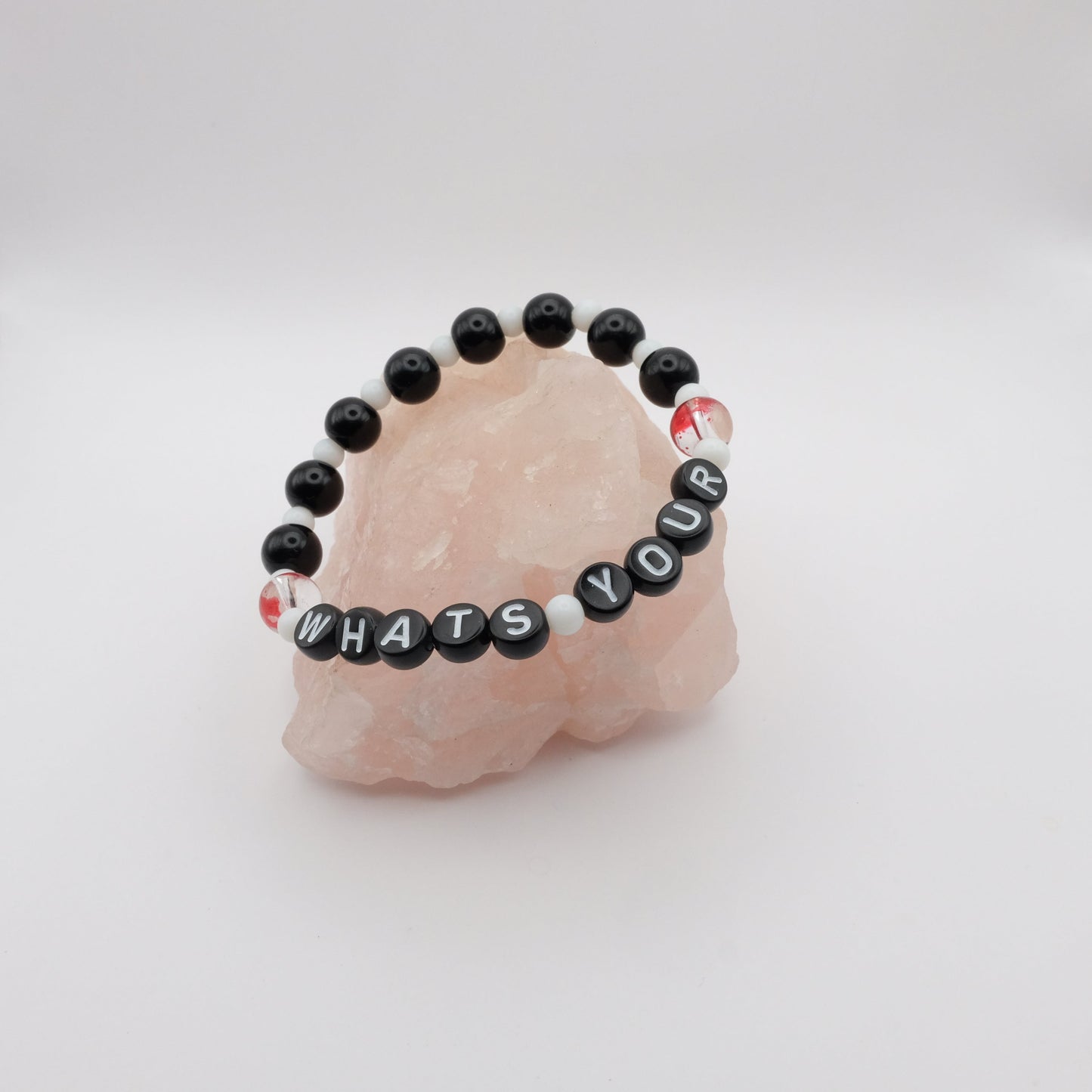Black beaded bracelet with letter beads spelling 'WHAT'S YOUR' on a pink stone with a white background