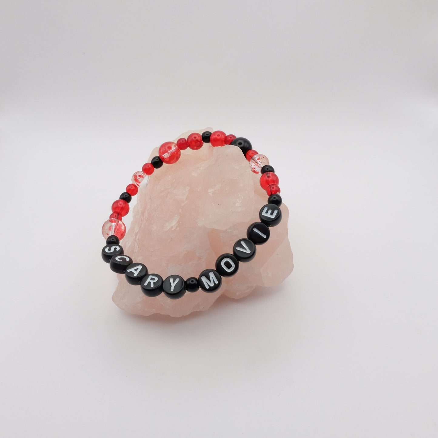 Bracelet with 'SCARY MOVIE' beads on a pink stone with a white background