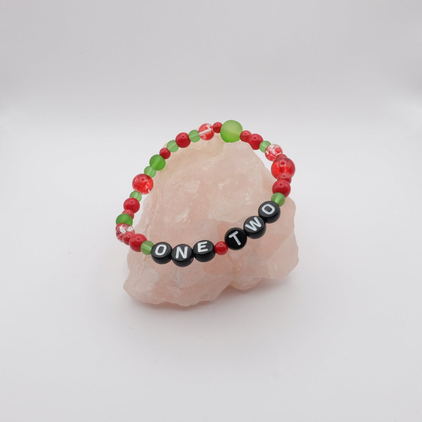 Bracelet with red, green, and black letter beads spelling "ONE TWO" on a white background