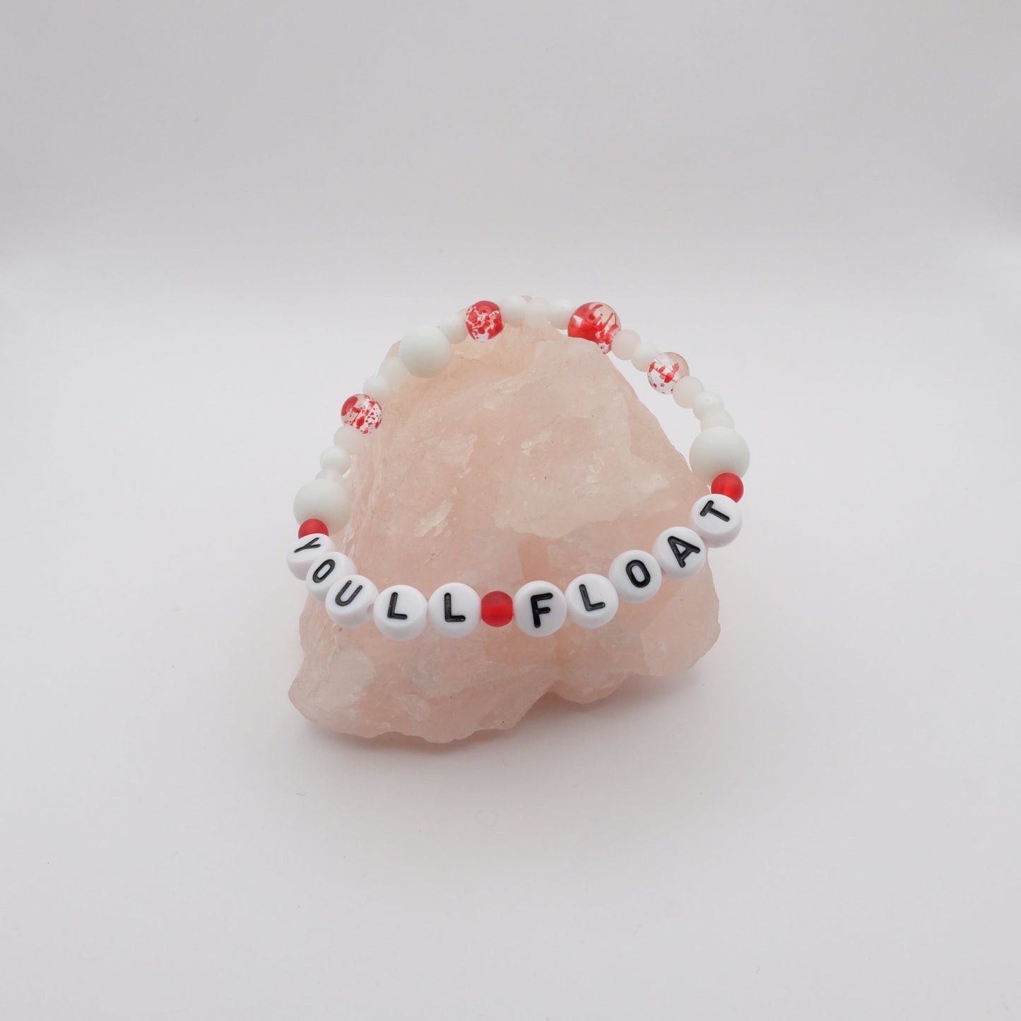 Pink stone with a 'YOU'LL FLOAT' bracelet on a white background