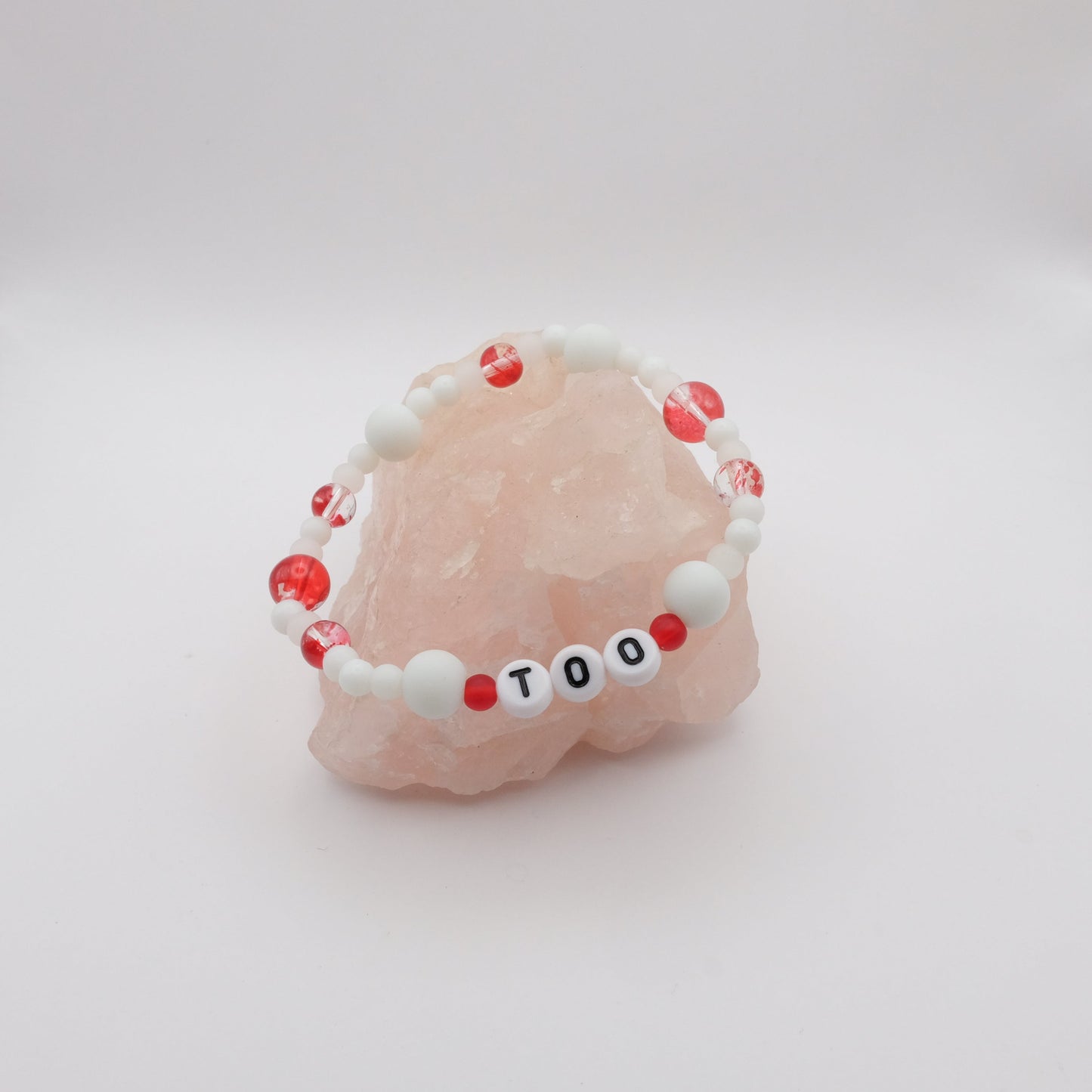 Bracelet with red and white beads and letter beads on a pink seashell against a white background