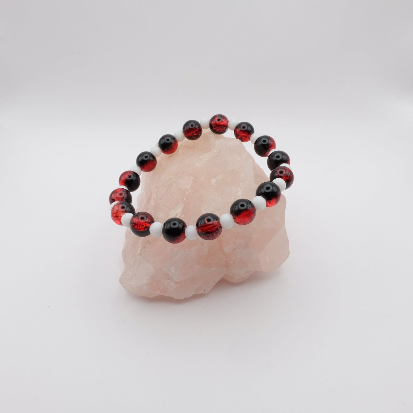 Beaded bracelet with red, black, and white beads on a pink stone against a white background