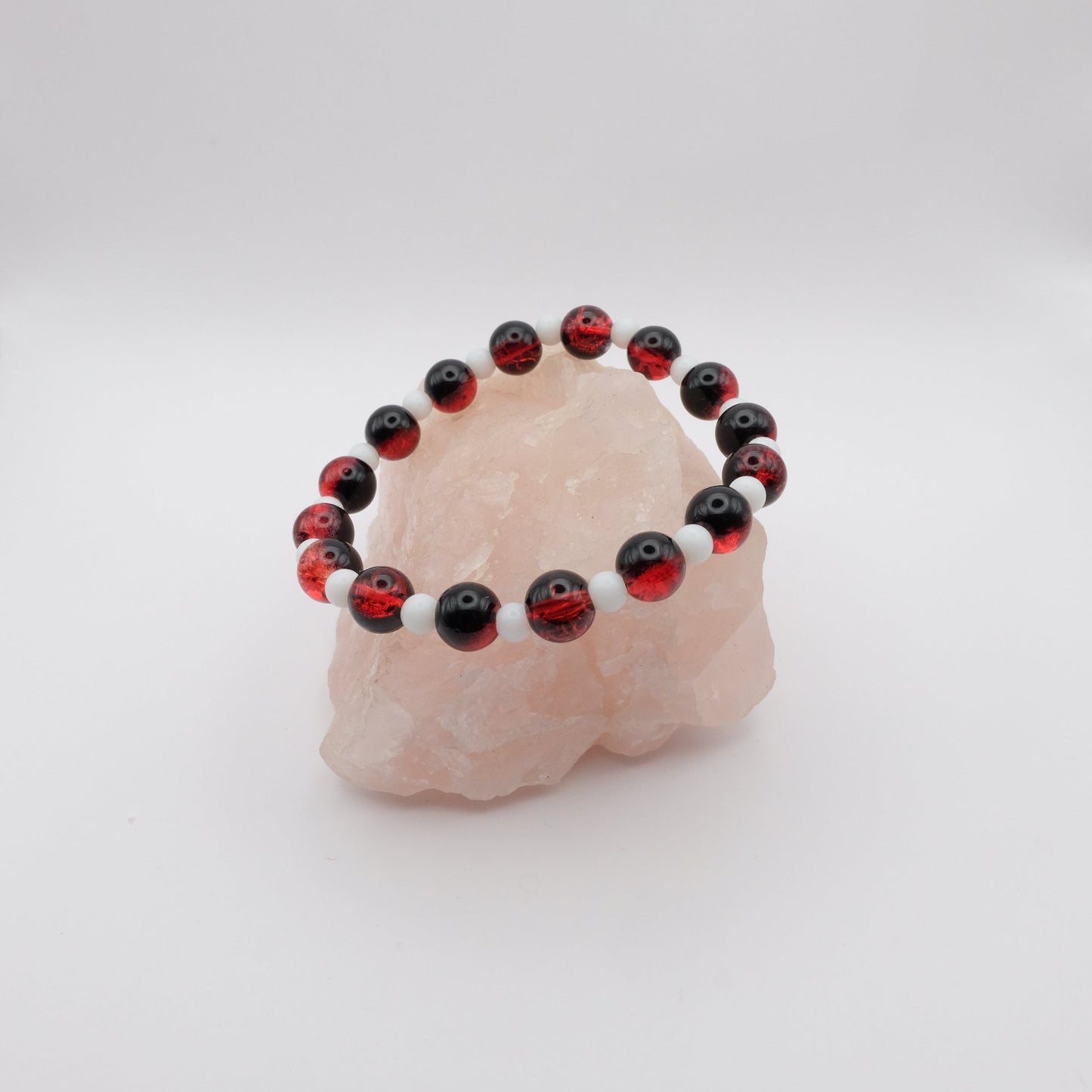 Beaded bracelet with red, black, and white beads on a pink stone against a white background