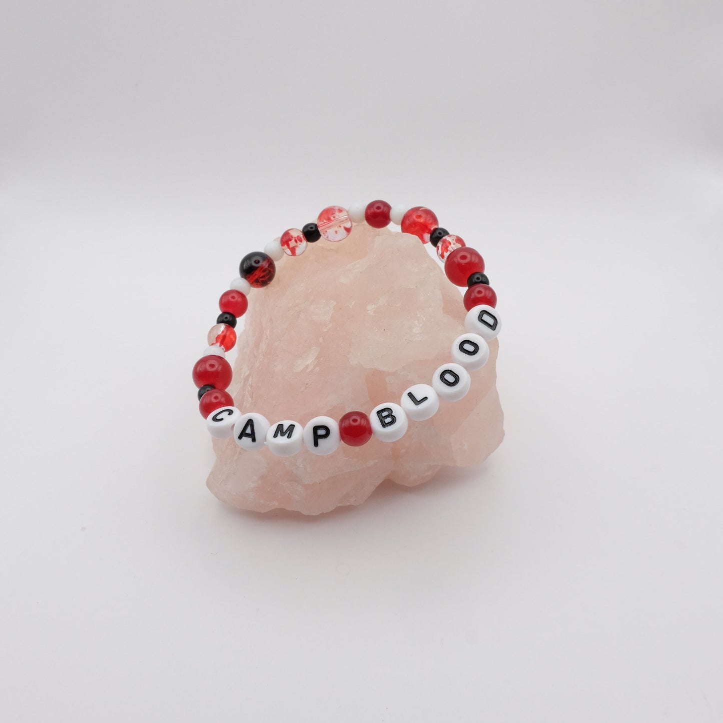 Bracelet with 'CAMP BLOOD' beads on a pink stone with a white background