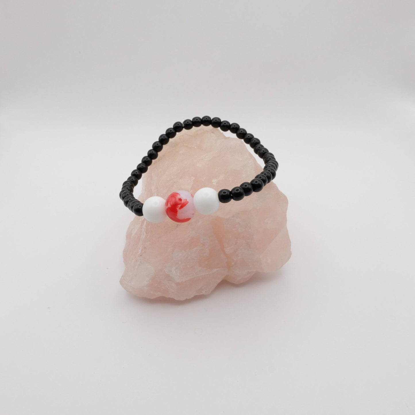 Black beaded bracelet with white and red accents on a pink stone against a white background