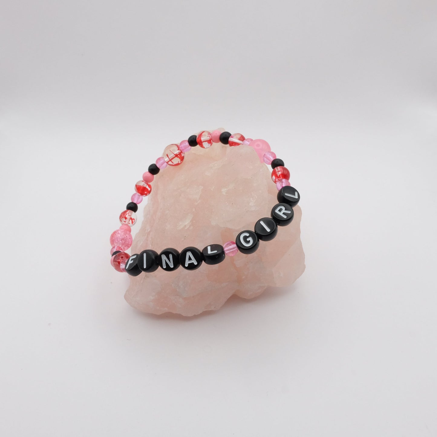 Bracelet with 'FINAL GIRL' beads on a pink stone with a white background