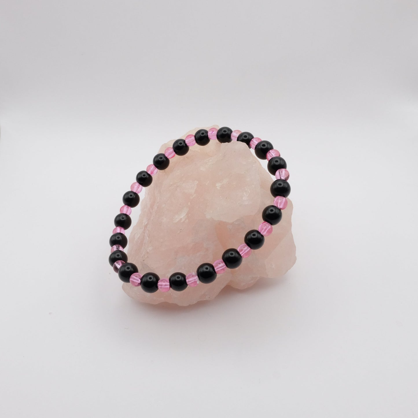 Black and pink beaded bracelet on a pink stone with a white background