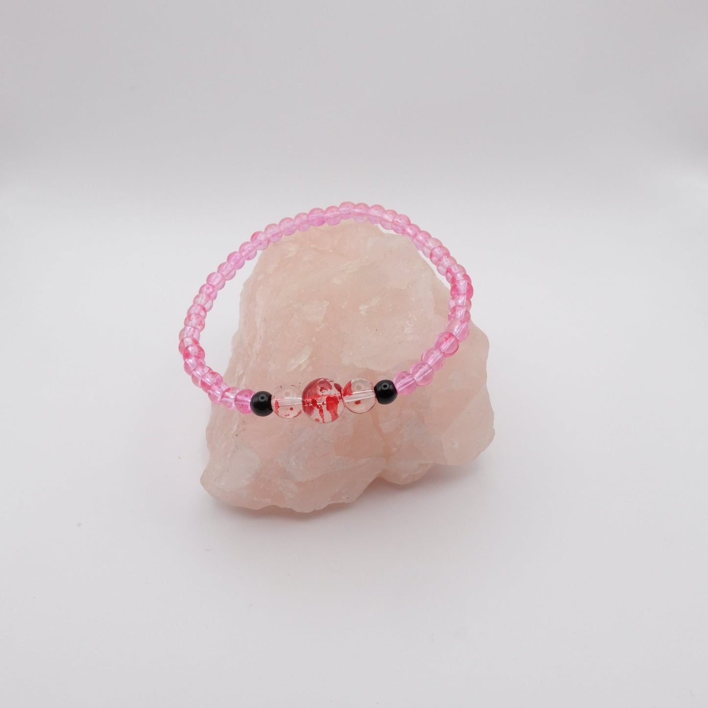 Pink beaded bracelet with black beads on a pink stone against a white background