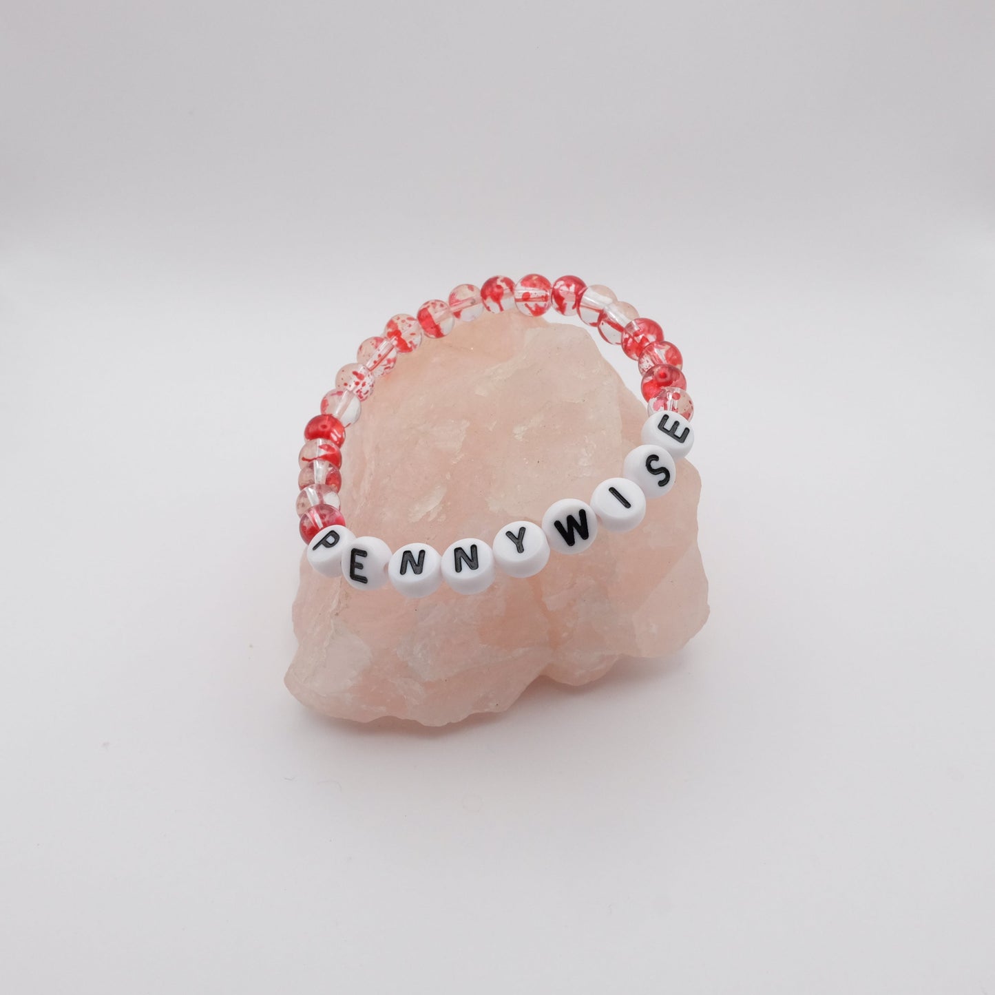 Pink stone with a beaded band labeled 'PENNYWISE' on a white background