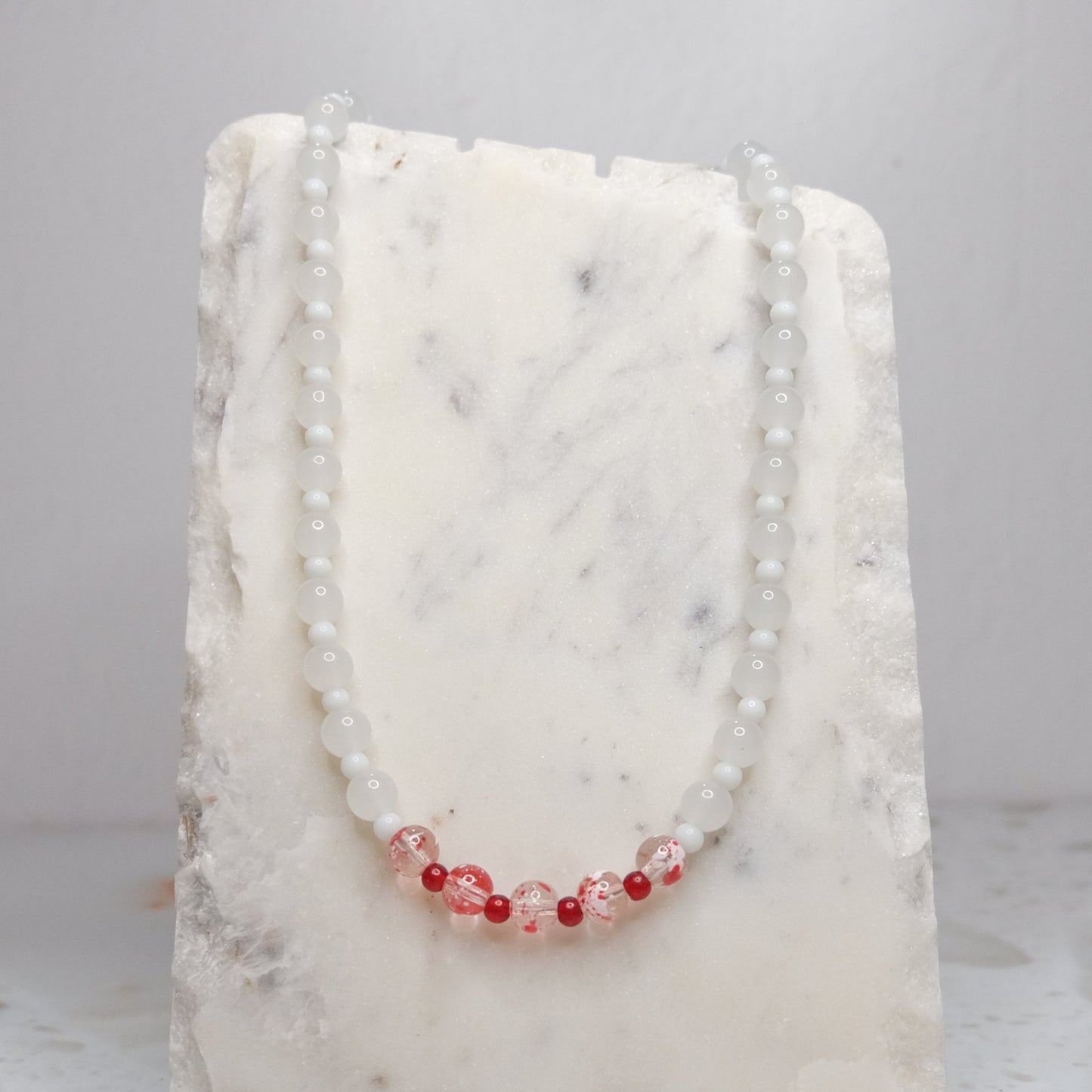 Necklace with white and red beads on a white stone surface