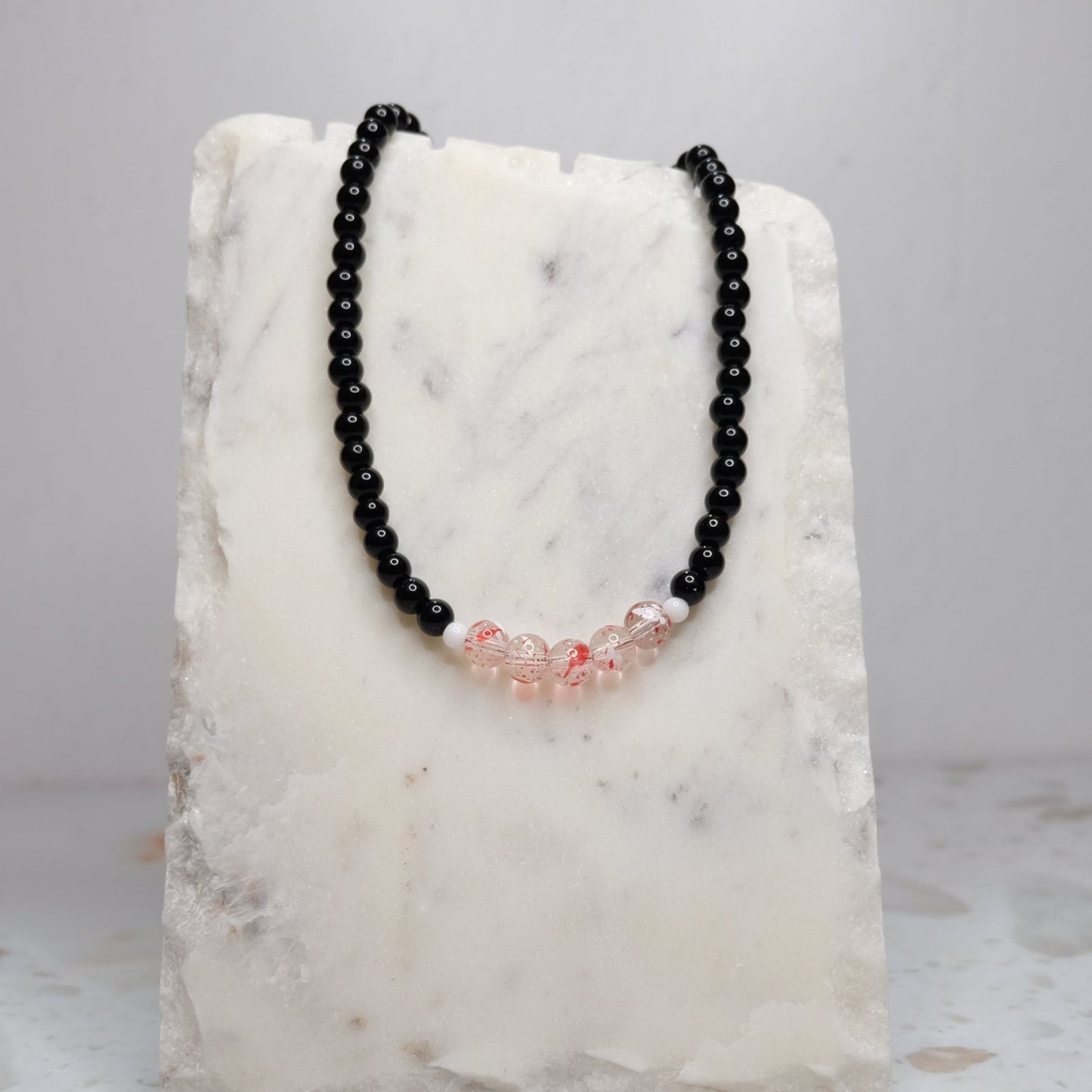 Black beaded necklace with red accents on a marble stand against a light gray background