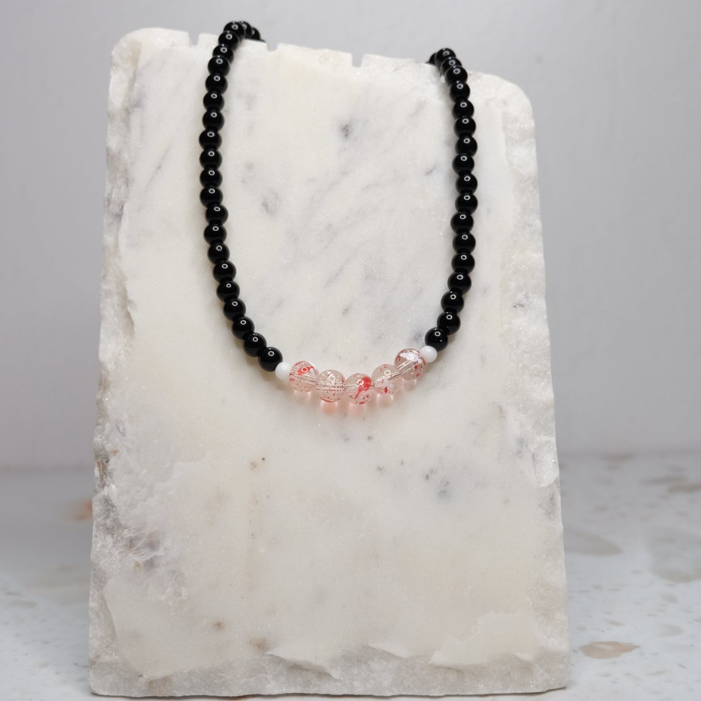 Black beaded necklace with red accents on a marble stand against a light gray background