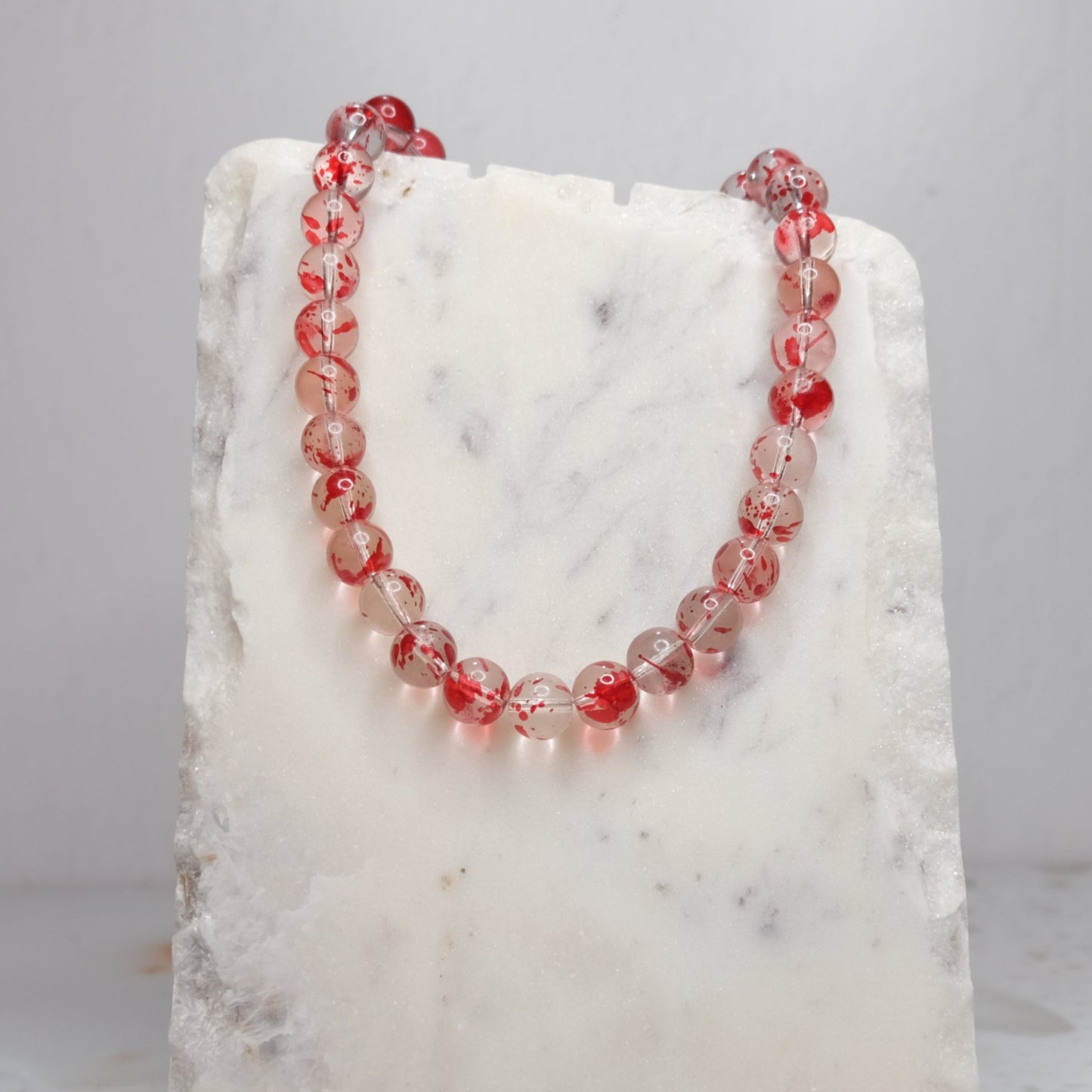 Necklace with red and clear beads on a white marble block against a light gray background