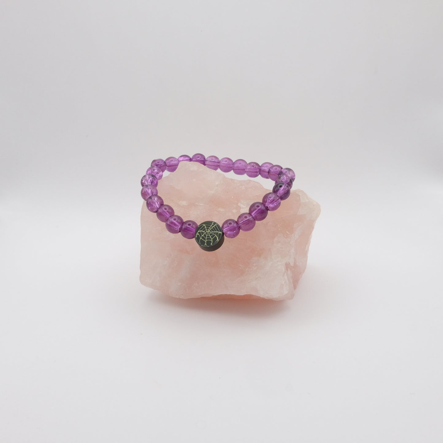 Purple beaded bracelet with a black spiderweb bead on a pink crystal against a white background