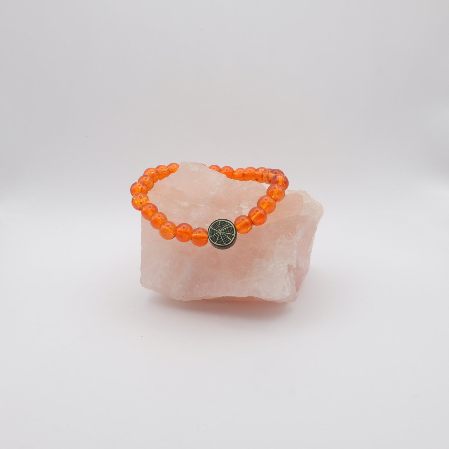 Orange beaded bracelet with a black spiderweb bead on a pink stone against a white background