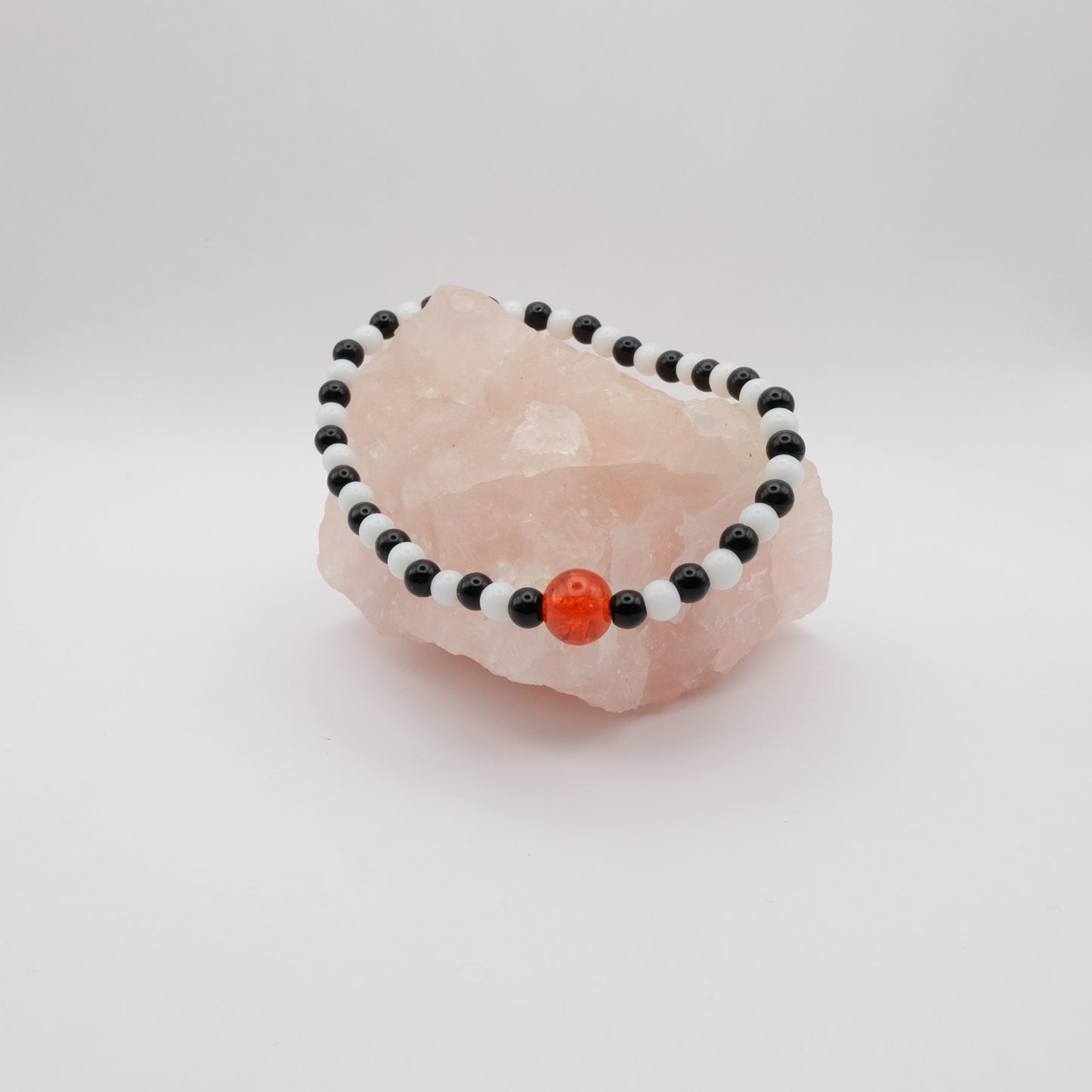 Beaded bracelet with black, white, and orange beads on a pink stone against a white background
