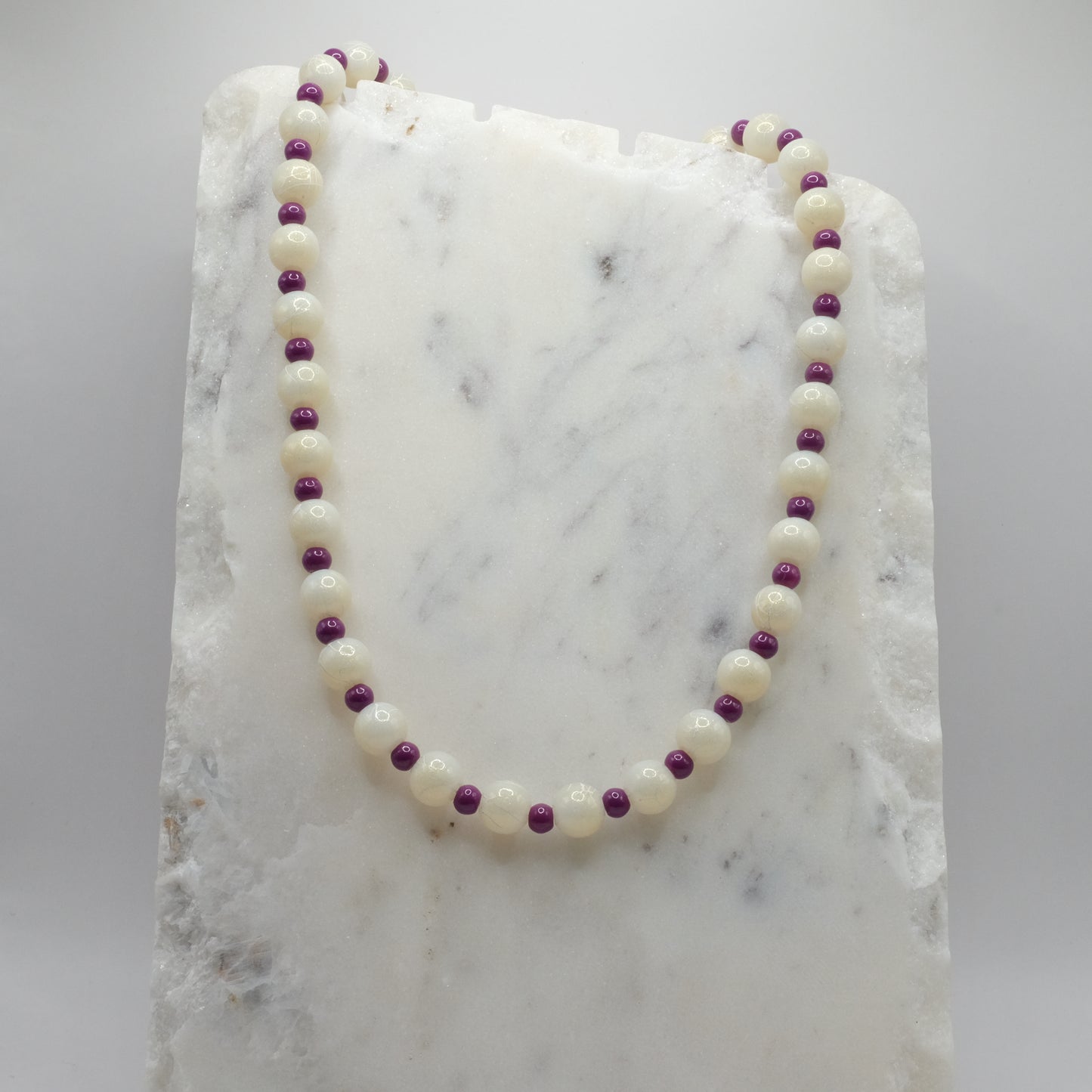 Necklace with white and purple beads on a marble surface