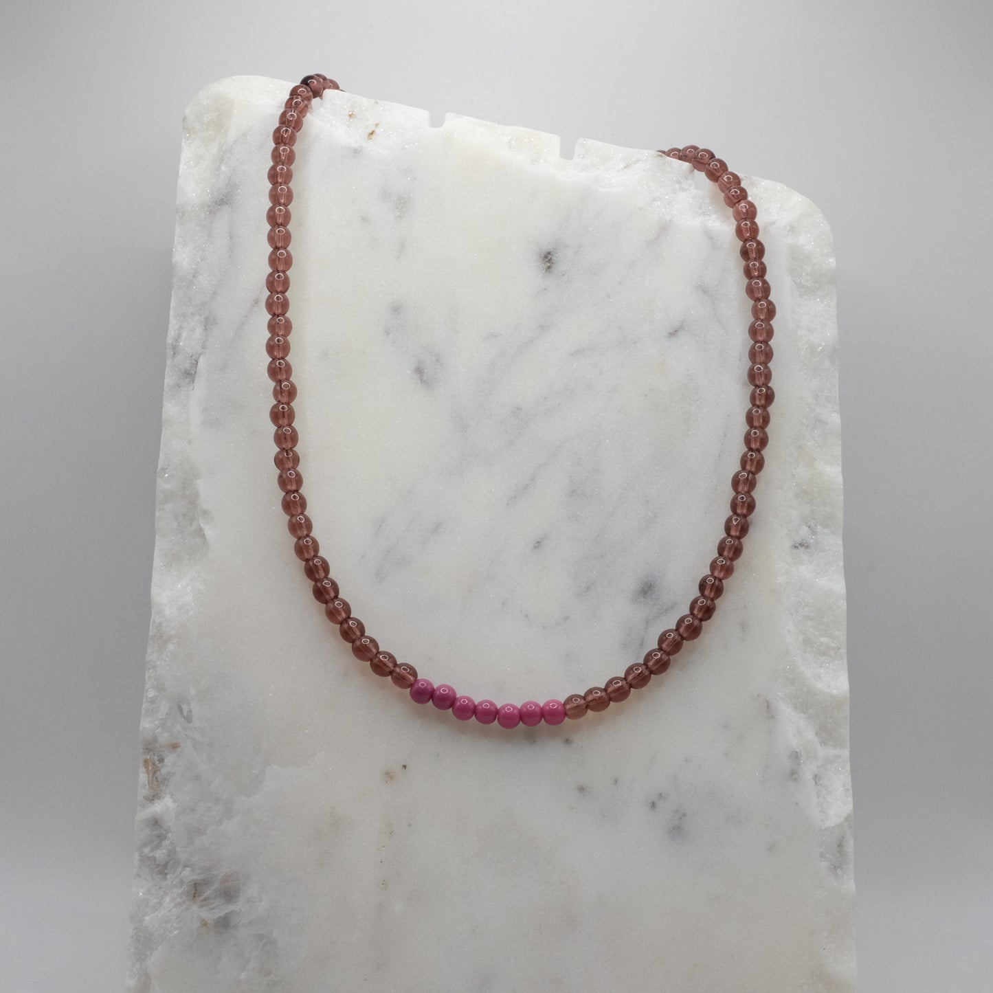 Beaded necklace with alternating red and pink beads on a marble surface