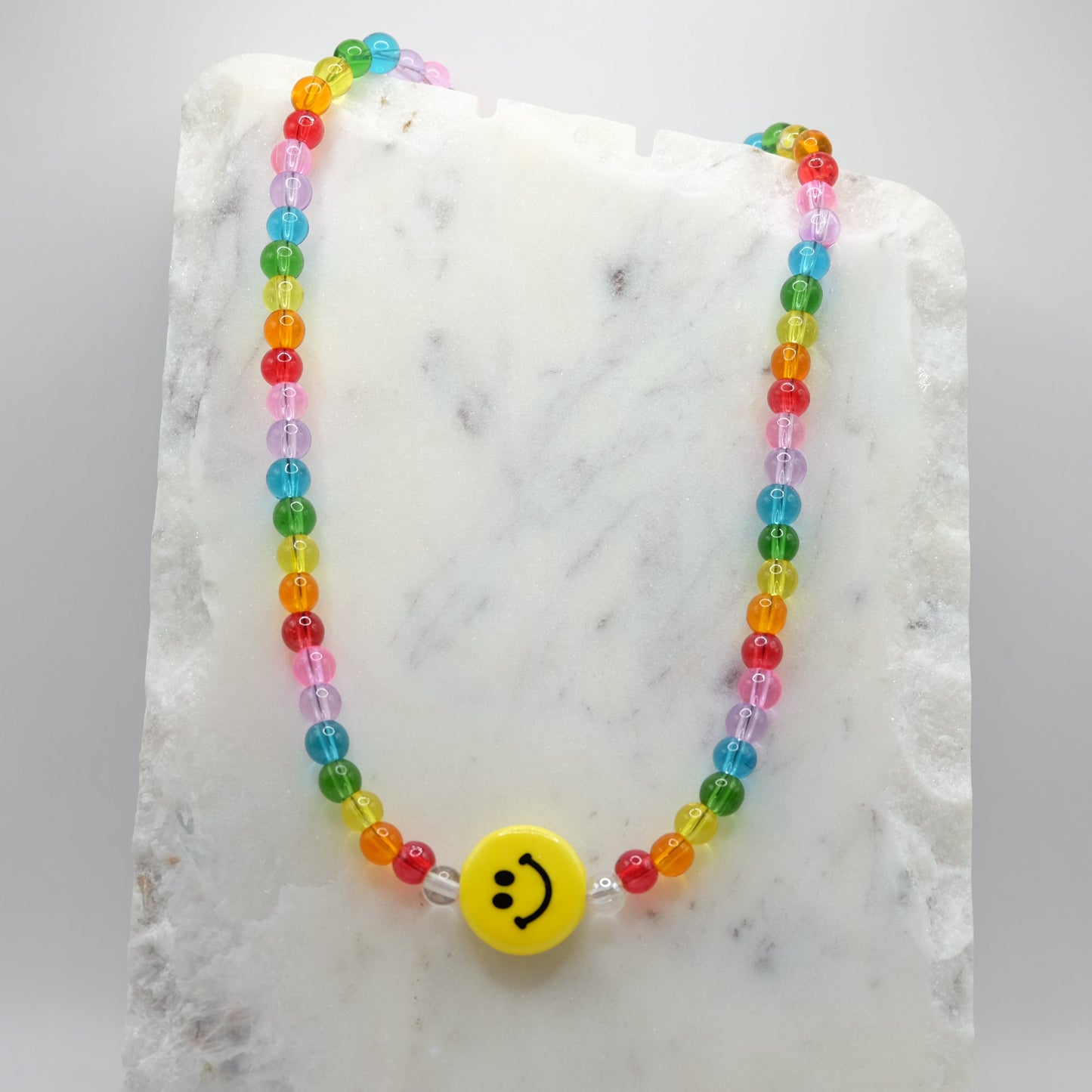 Rainbow beaded necklace with a ceramic smiley face bead on a marble surface