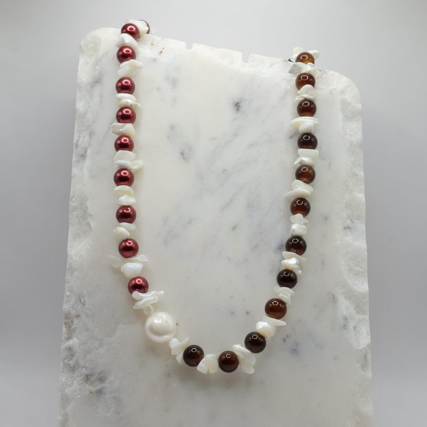 Necklace with red, brown, and white beads on a marble surface
