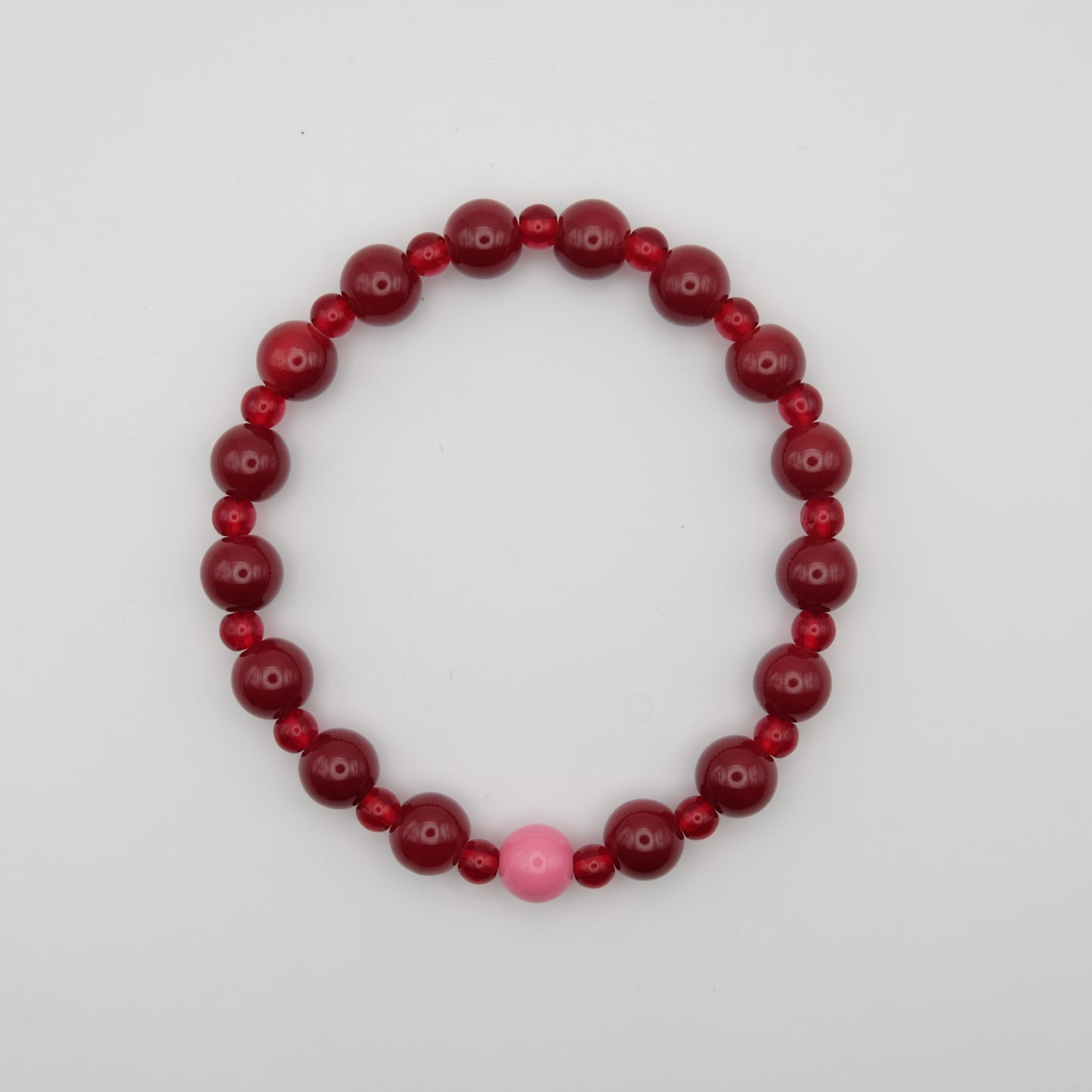 Beaded bracelet with red and pink beads on a plain background