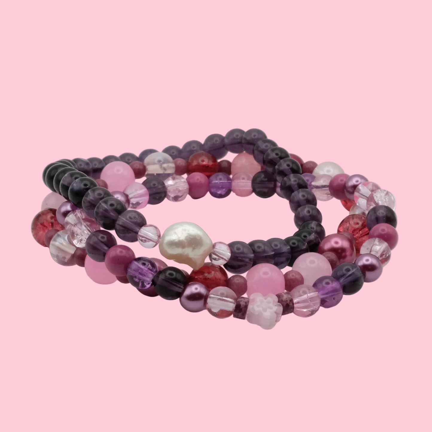 One-of-a-kind bracelet stack featuring pink, purple and berry-toned glass beads, floral accents and crystal details.