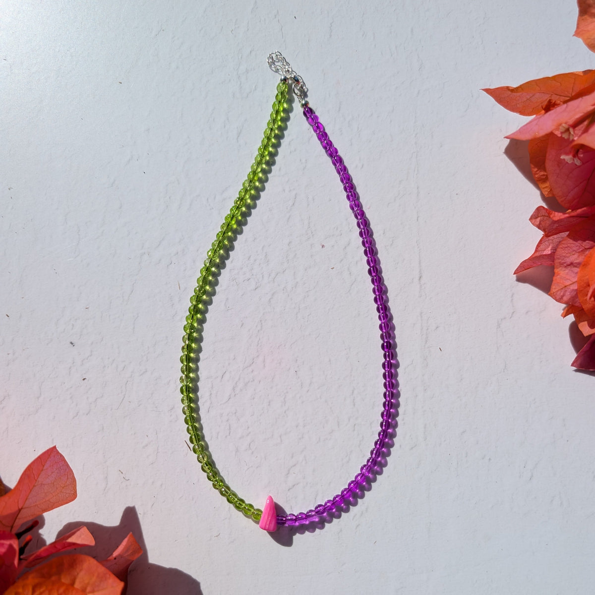 Handmade two-tone beaded necklace with green and purple glass beads and a single bright pink shell chip at the centre.