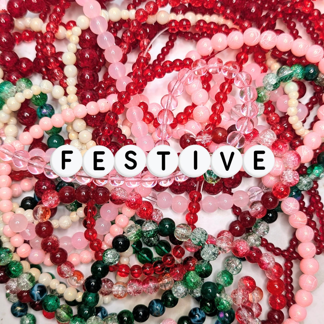 festive shades of pink, red, green, white, and clear. Across the centre, white acrylic letter beads spell “FESTIVE.” The background is softly lit, highlighting the holiday-inspired colour palette.