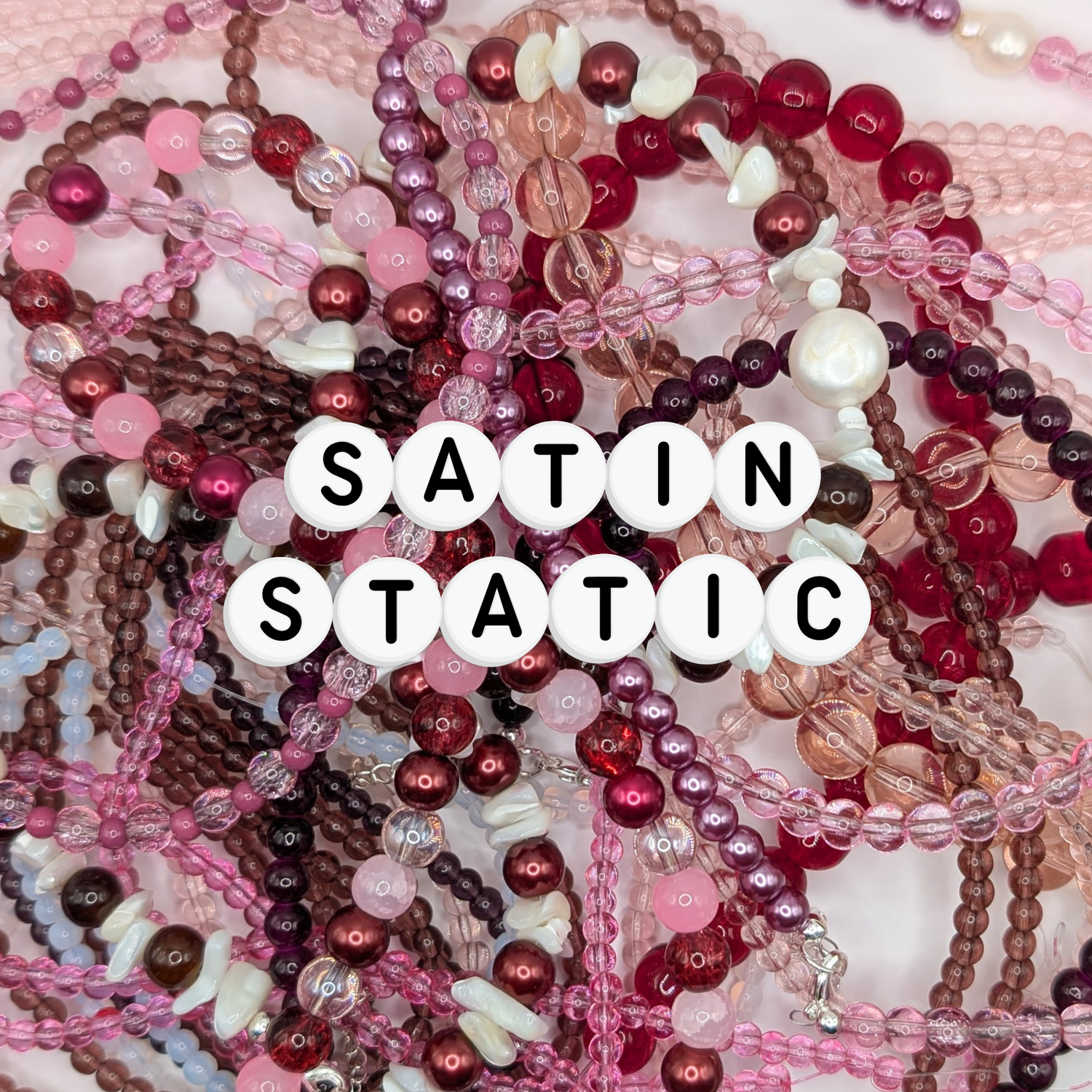 A flat lay of handmade beaded jewellery featuring glass beads, freshwater pearls and pink, plum and red tones, representing the Satin Static jewellery collection.