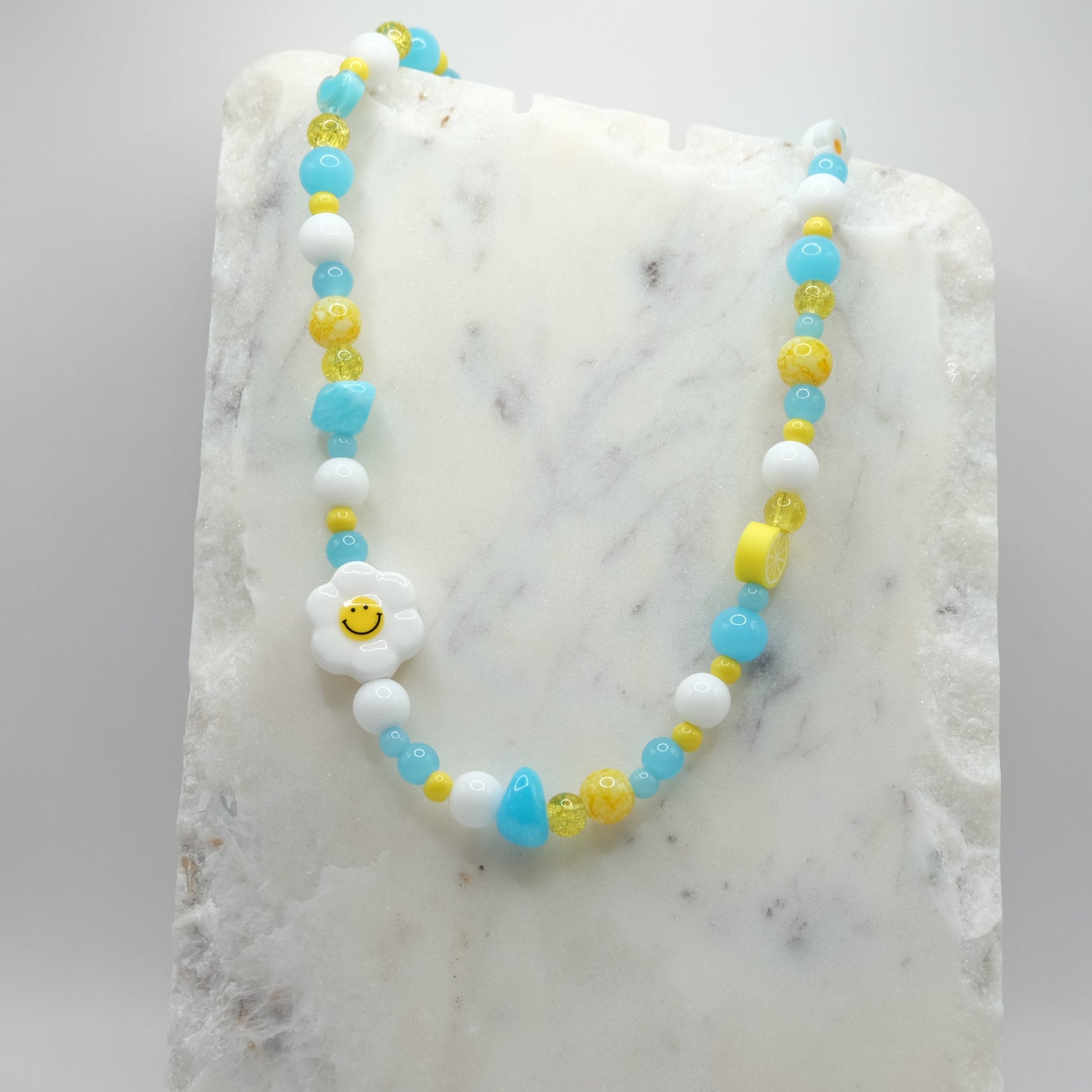 Beaded necklace with a smiley face charm on a marble surface