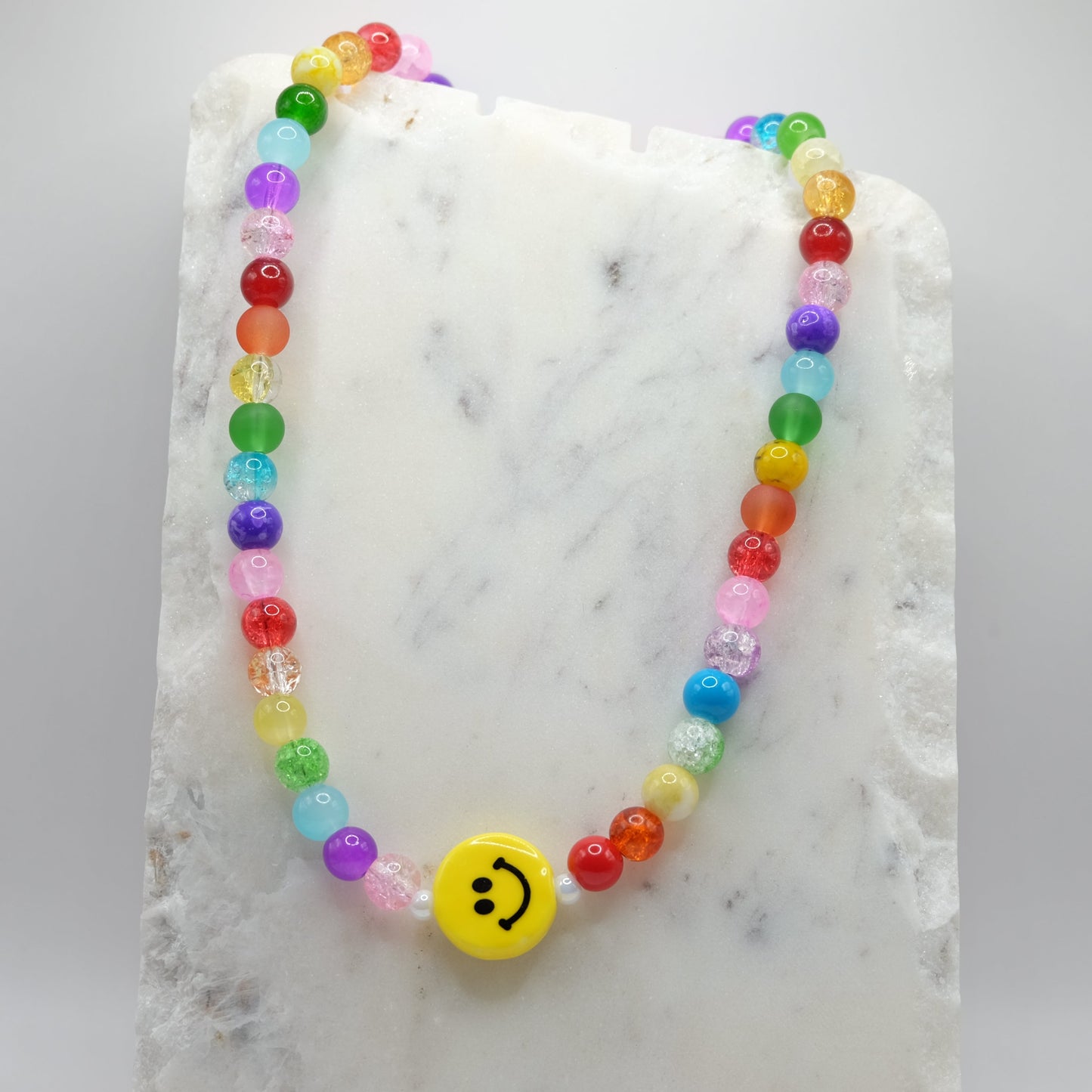Colorful beaded necklace with a smiley face charm on a marble surface