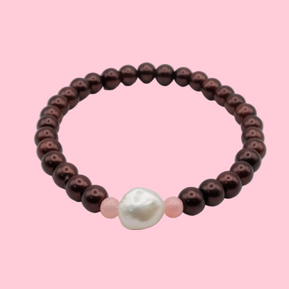 An elastic beaded bracelet composed of metallic burgundy pearl-finish 8mm glass beads featuring a freshwater pearl centrepiece with soft pink accent beads, shown on a white background.