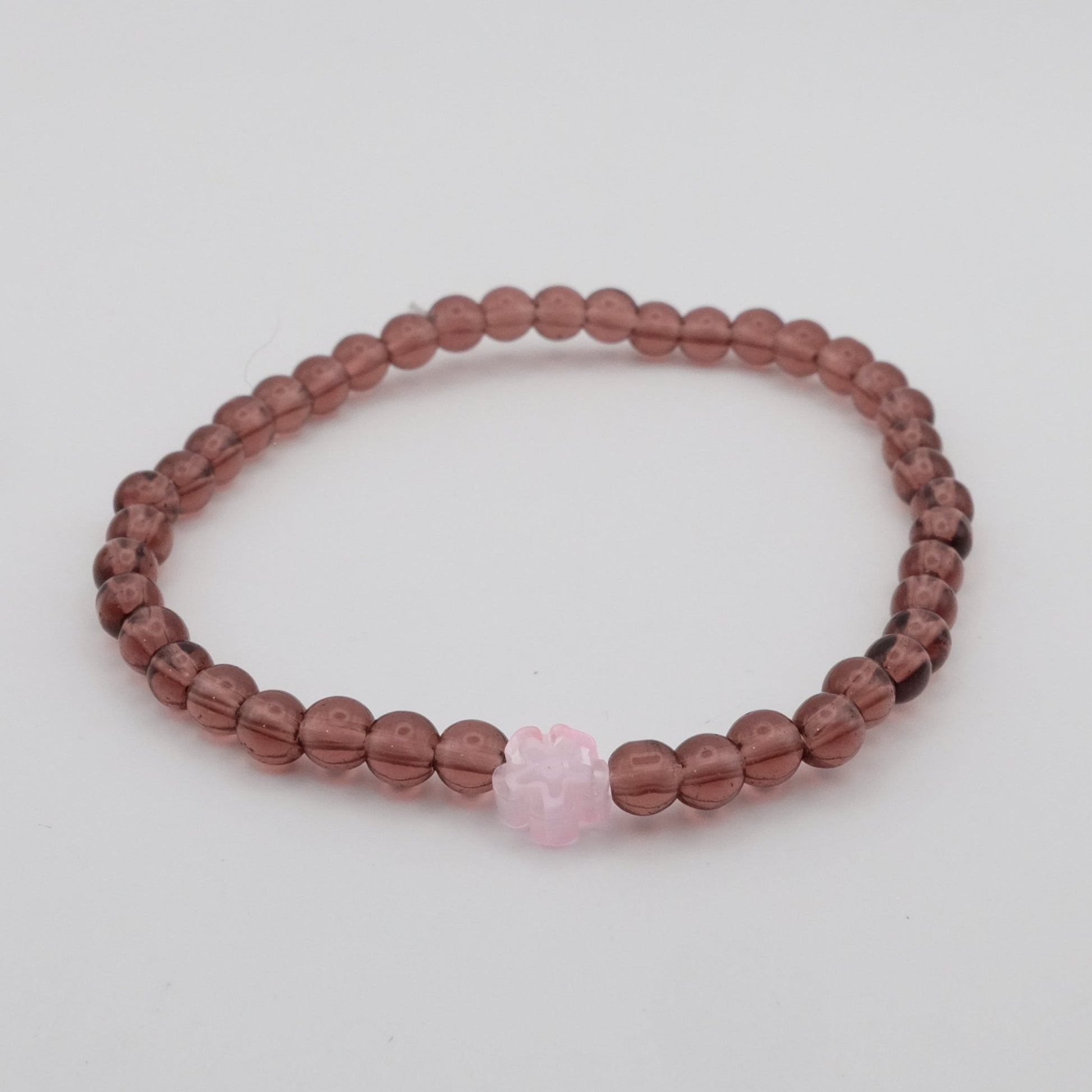 Beaded bracelet with a pink heart charm on a light gray background