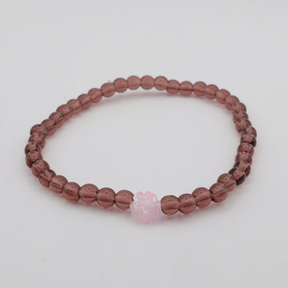 Beaded bracelet with a pink heart charm on a light gray background